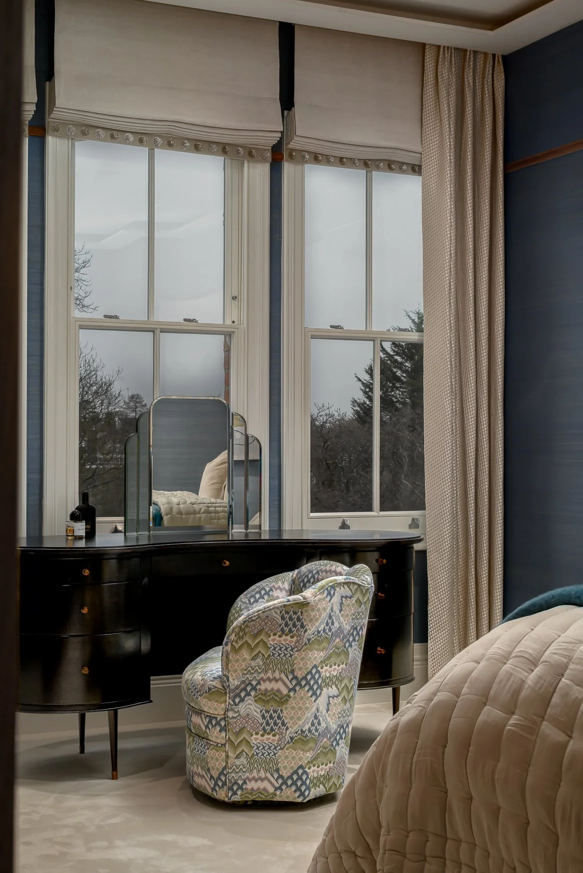 Dressing table, patterned chair and tall windows in a bespoke bedroom scheme.