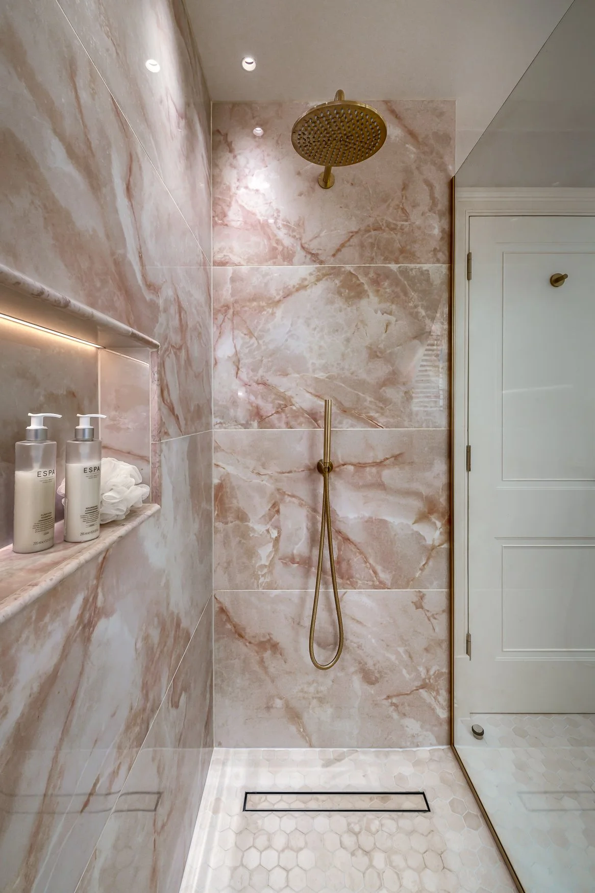 Pink marble-effect shower with brass fittings, glass screen and illuminated recessed shelf.
