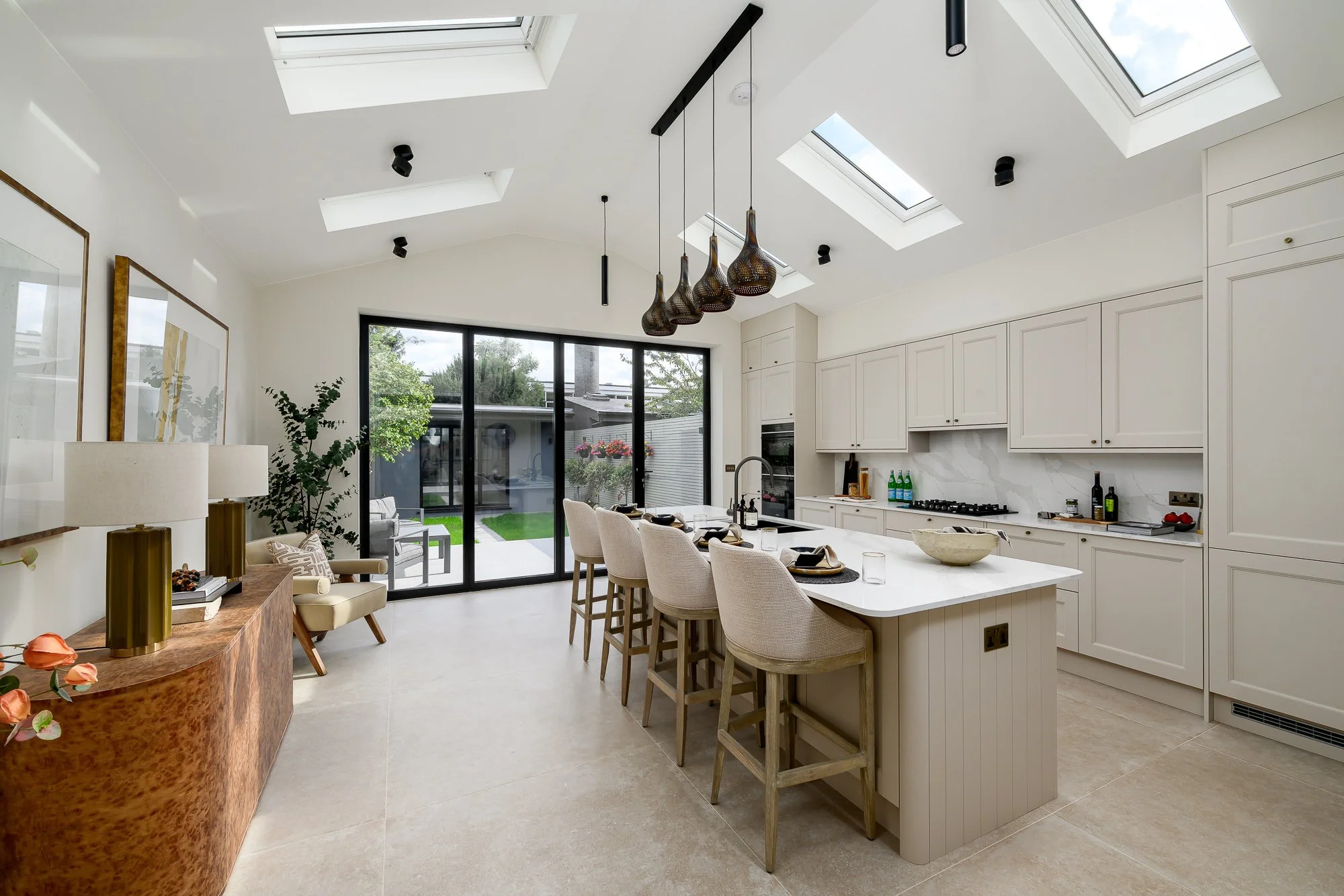 Interior architecture photography of a light-filled kitchen extension with skylights, full-height garden glazing, bespoke cabinetry and a large kitchen island.