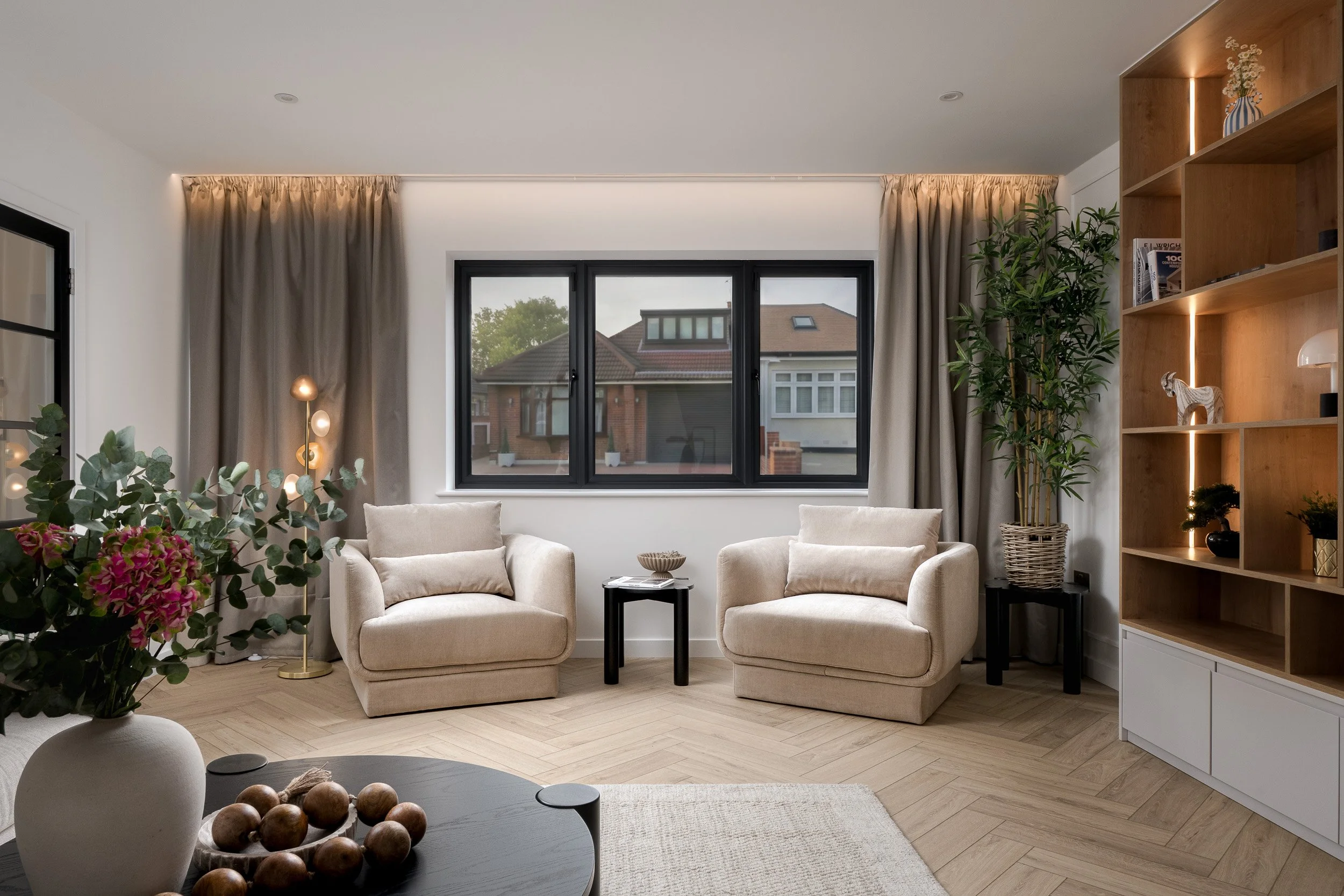 Contemporary living room with neutral furniture, bespoke shelving, large window and layered interior styling.