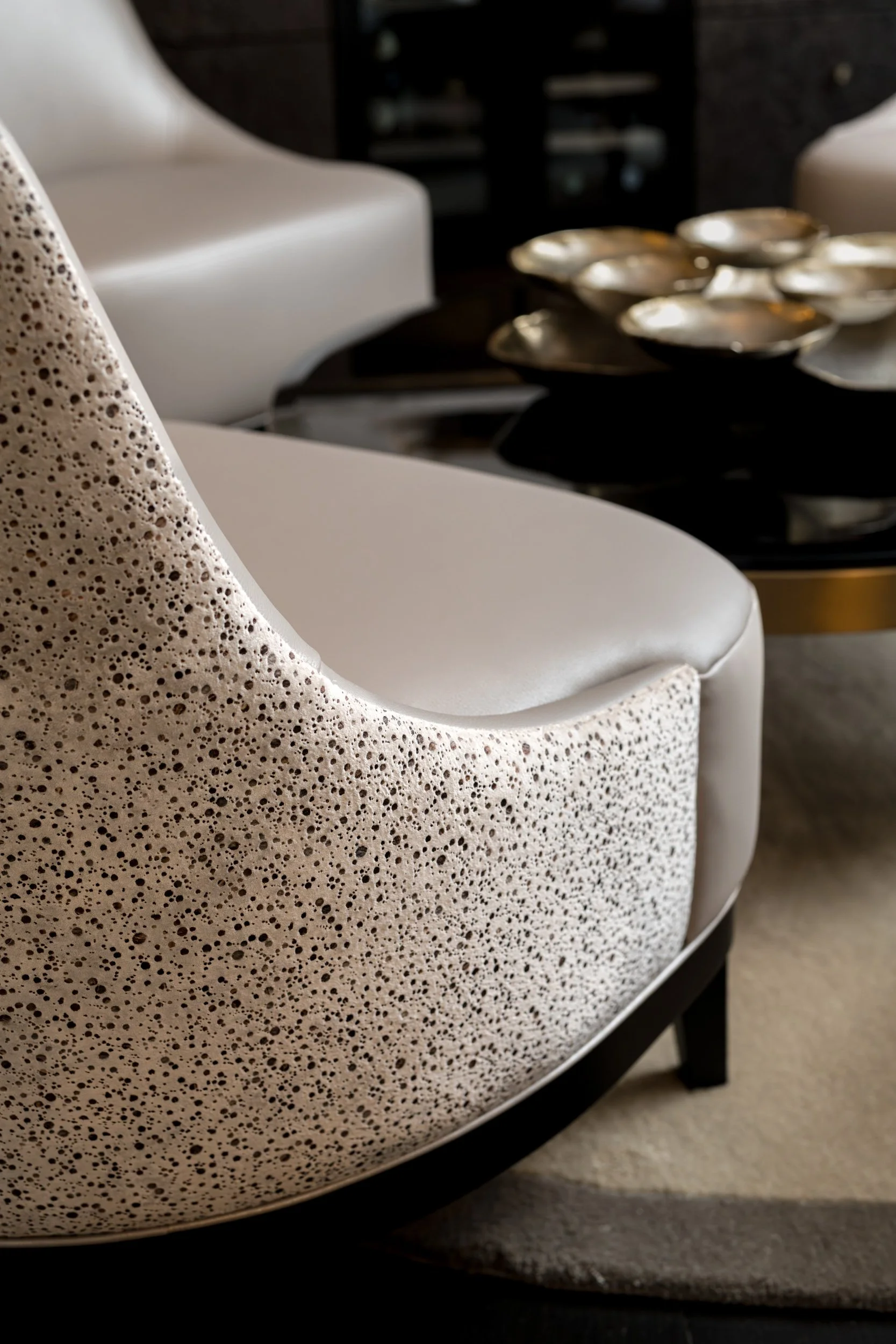 Close-up photo of a modern armchair with a speckled cream and black fabric, and a side table with decorative metallic bowls.