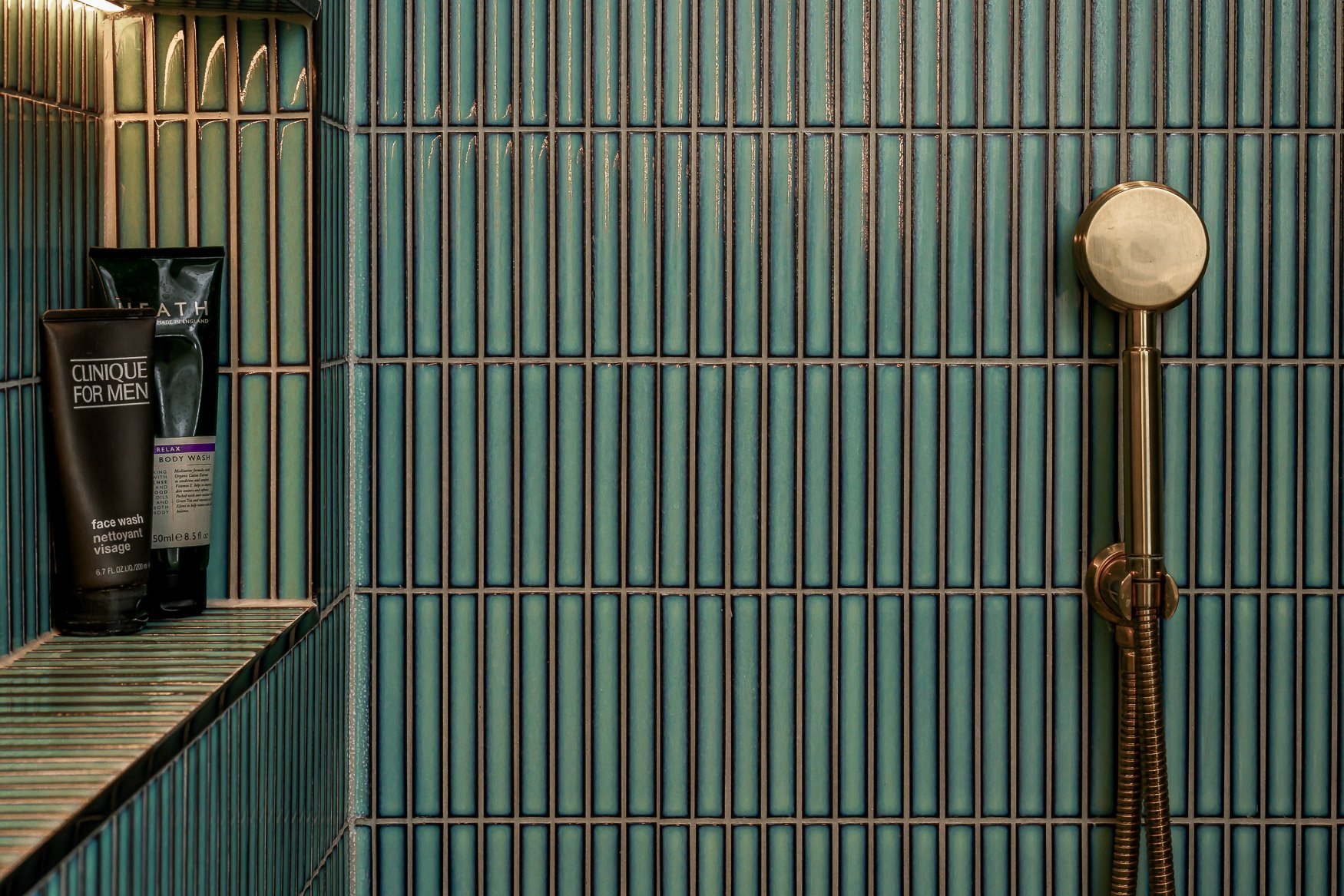 Green tiles in the shower with a nieche and brass finishes