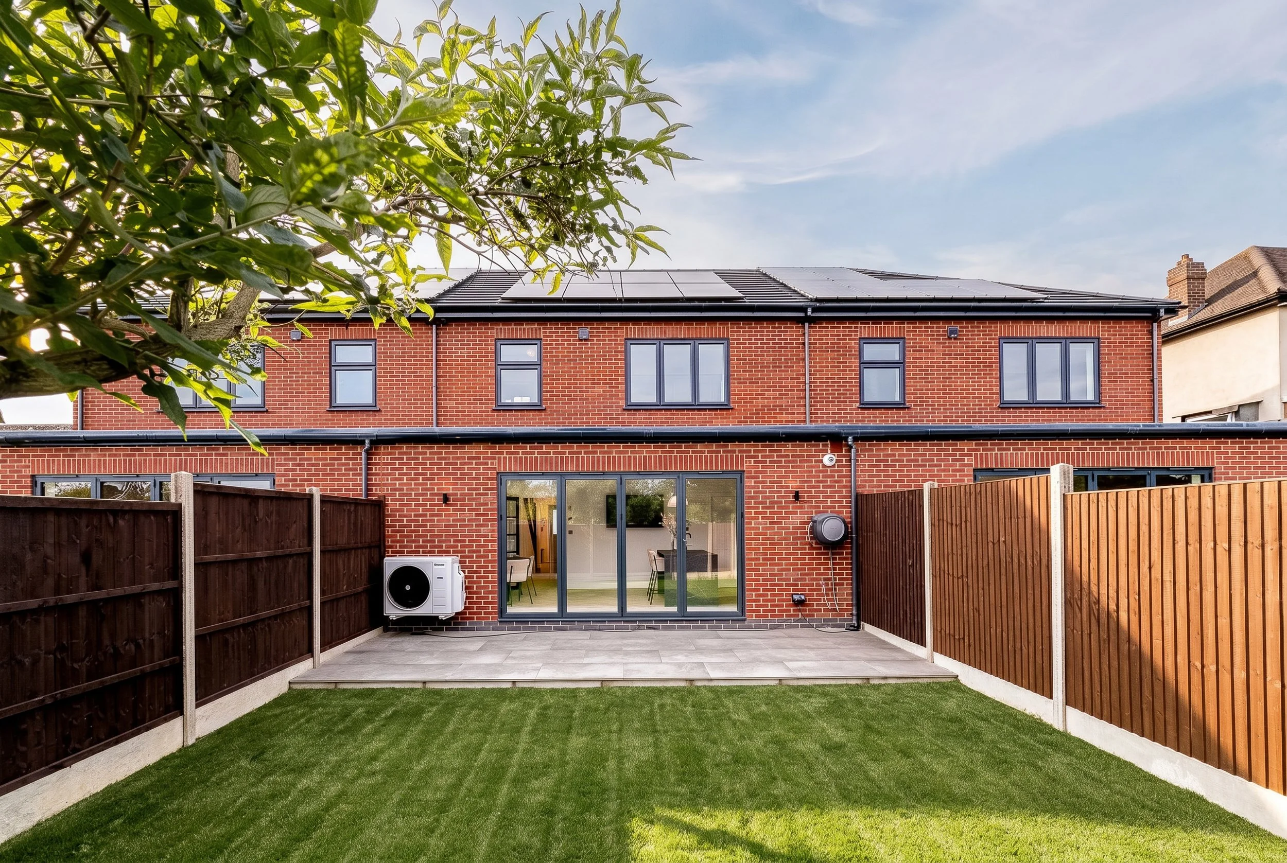 Detail exterior architectural photograph capturing the high-spec building envelope of a modern multi-unit residential development. Shot for main contractors and architectural firms to document external construction quality, featuring crisp red facing