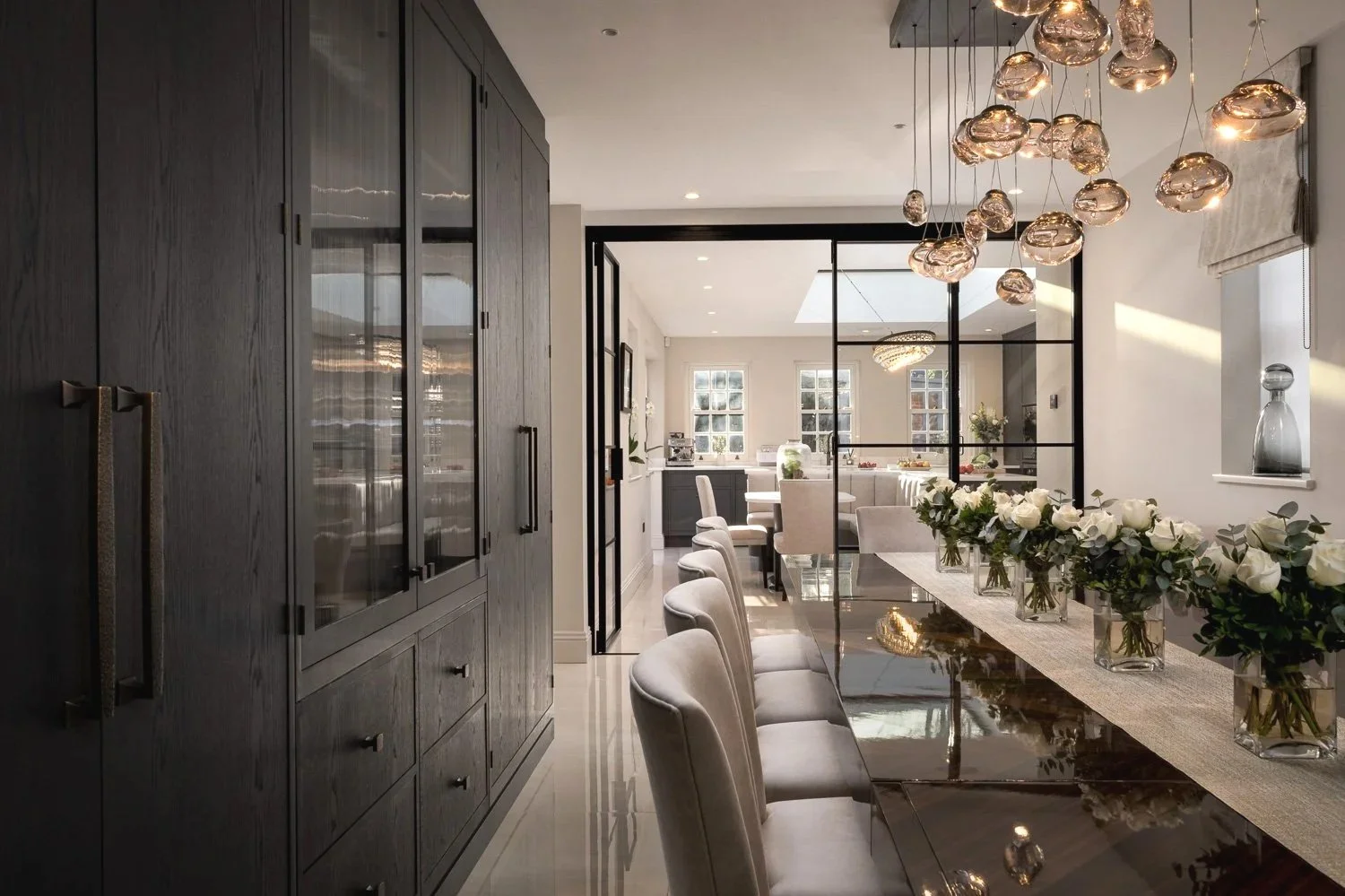Luxury modern dining and kitchen interior of a private Hampstead residence, photographed for architectural portfolio use — showcasing bespoke joinery, floral styling, and glass pendant lighting with homeowner consent.
