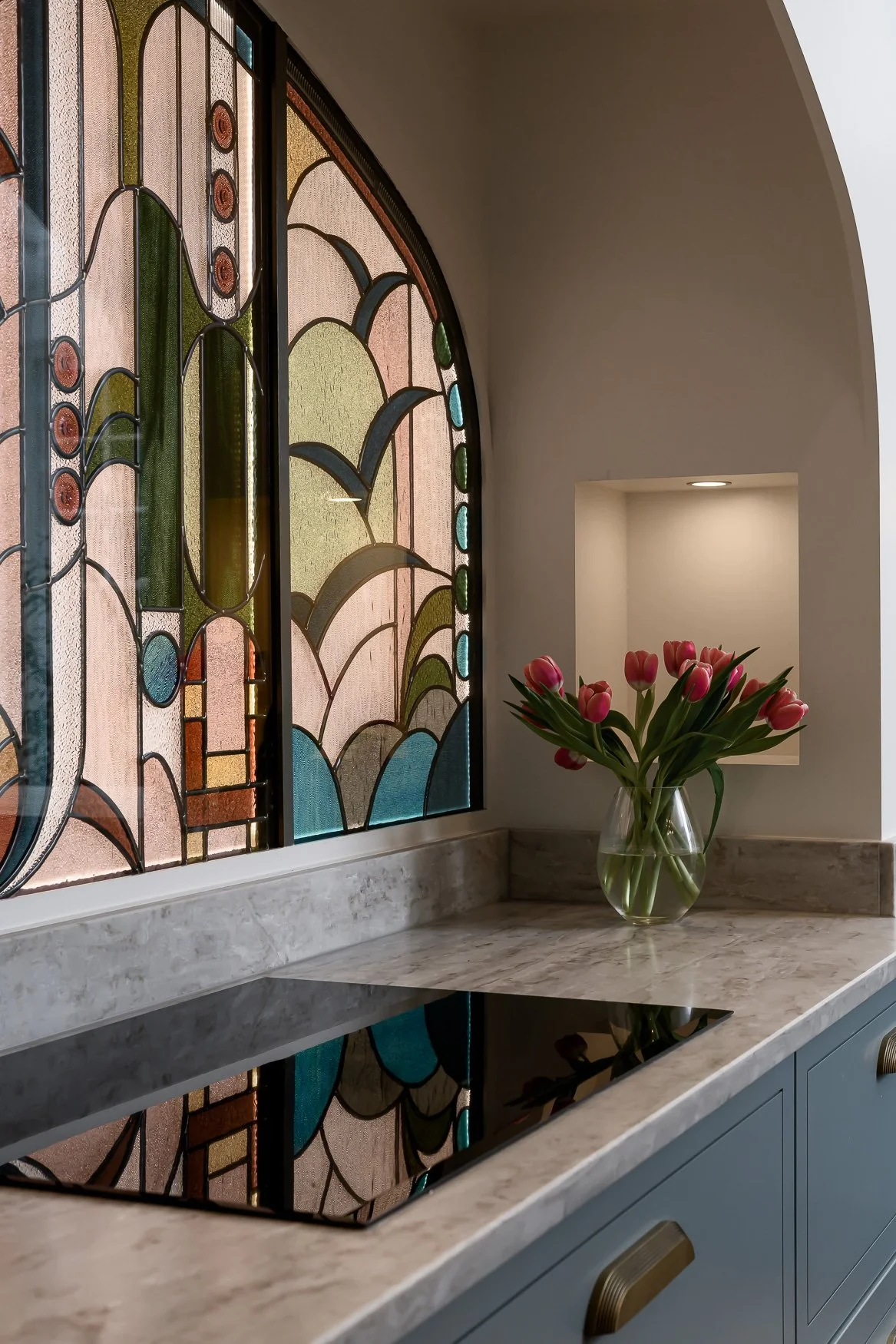 Bespoke kitchen with statement pendant lights, island seating and colourful stained glass backdrop.