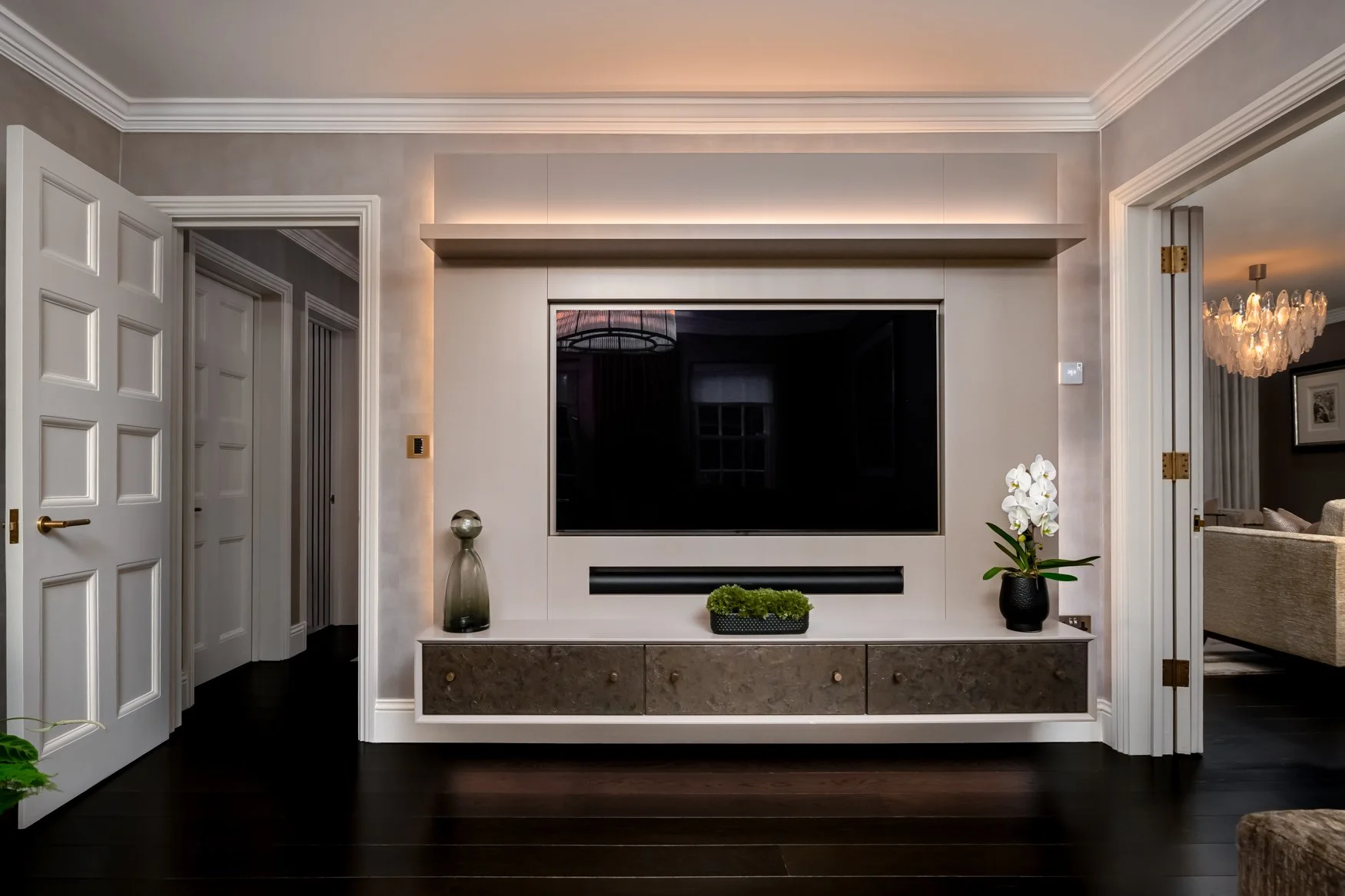 Living room with wall-mounted flat-screen TV, decorative vases, orchid plant, and cabinet, with open doorways to other rooms.