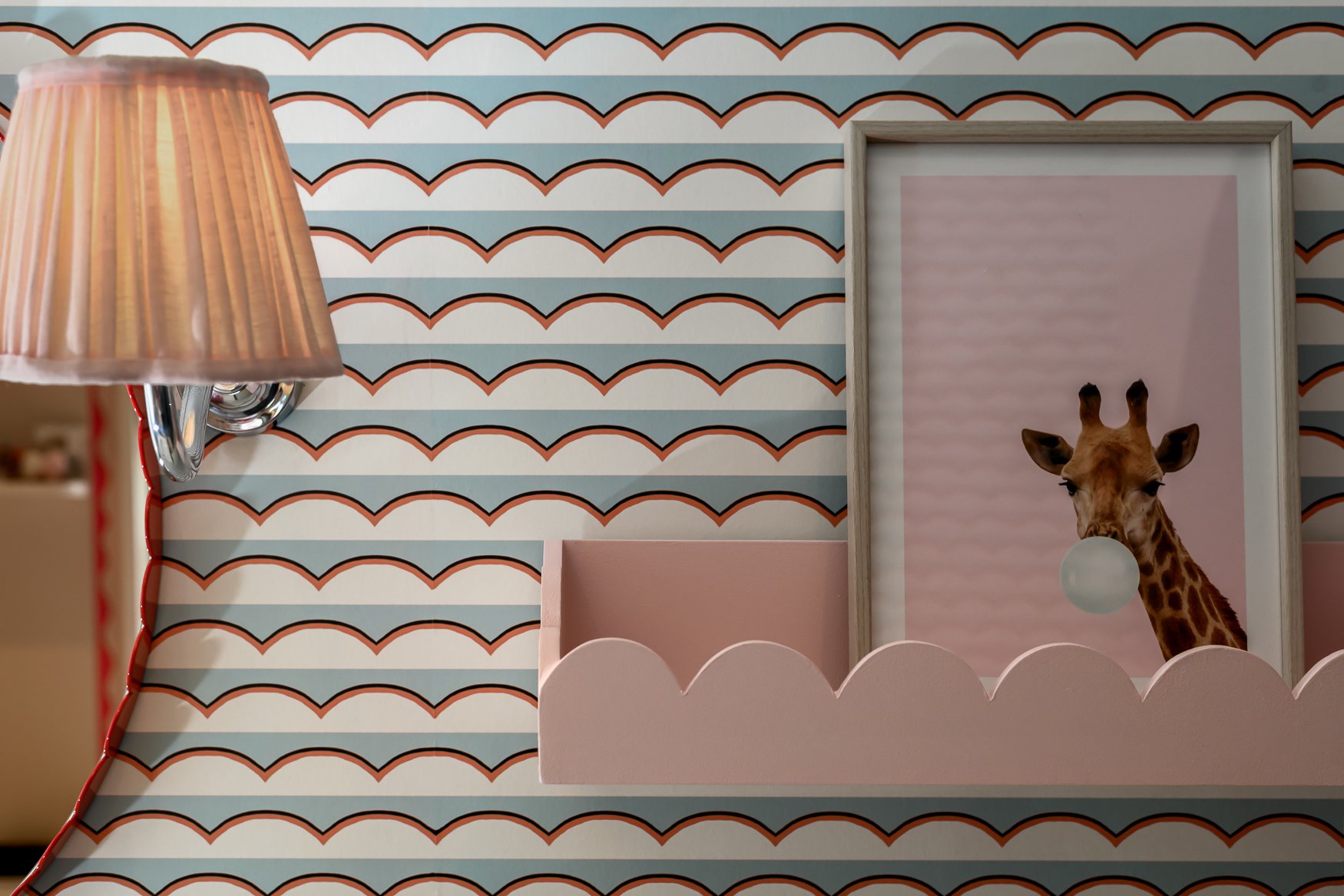 Decorative wall with a pink frame featuring a giraffe blowing a bubble, pink and white clouds in a furniture setting, and a warm lamp in a cozy room.