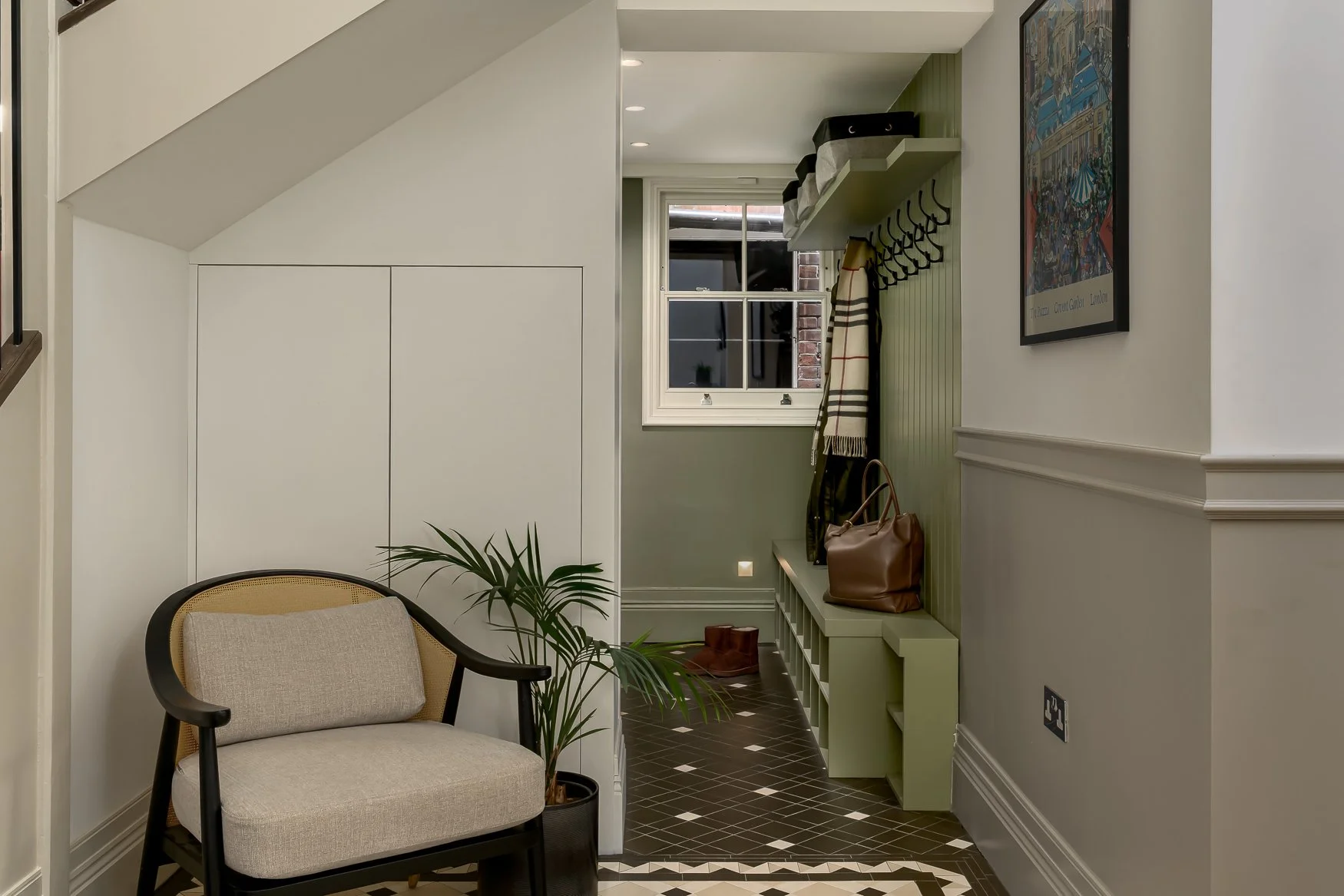 Boot room with soft green joinery, dark tiled floor and practical family storage.