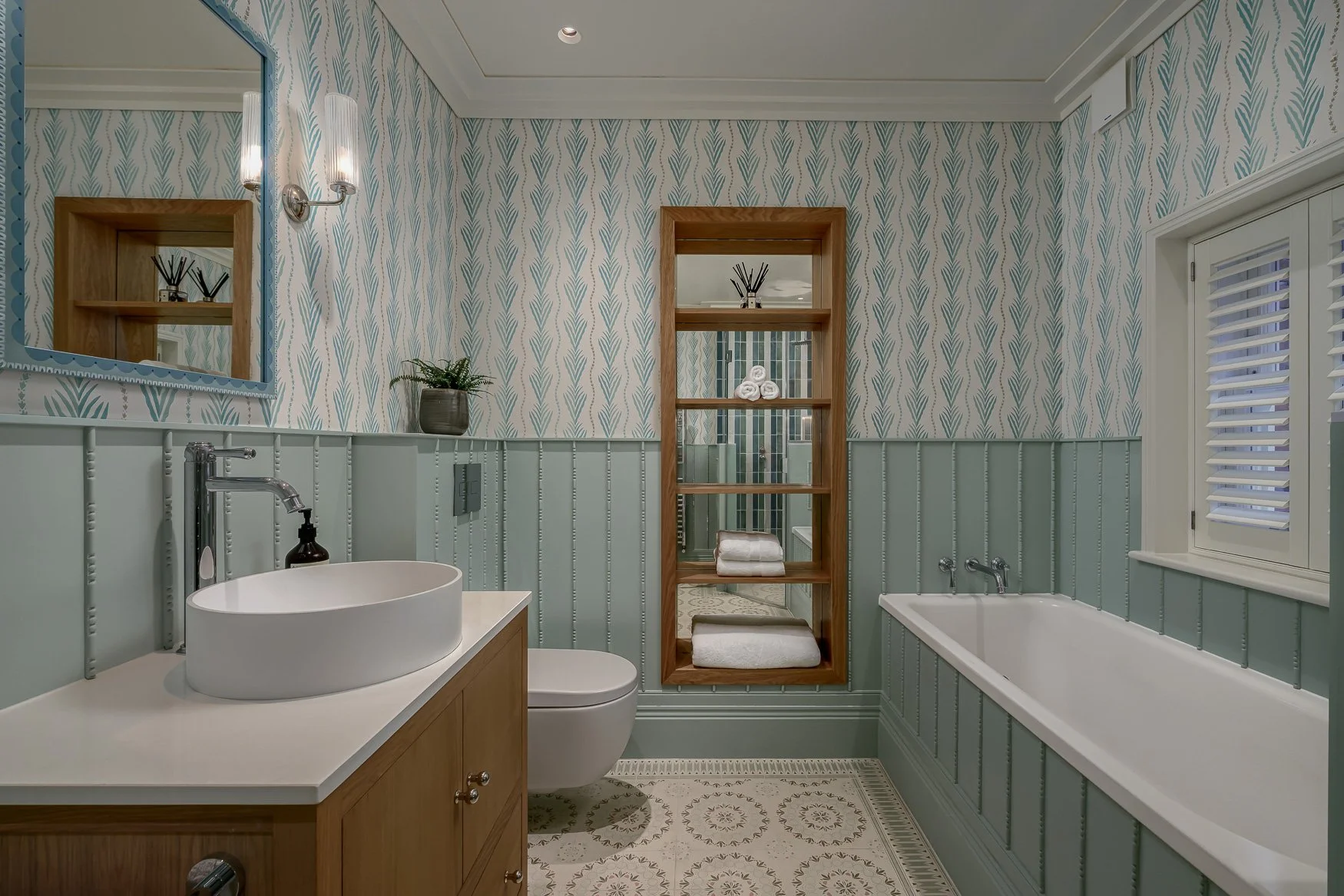 Family bathroom showing bath, shower enclosure, patterned floor tiles and soft green panelling.