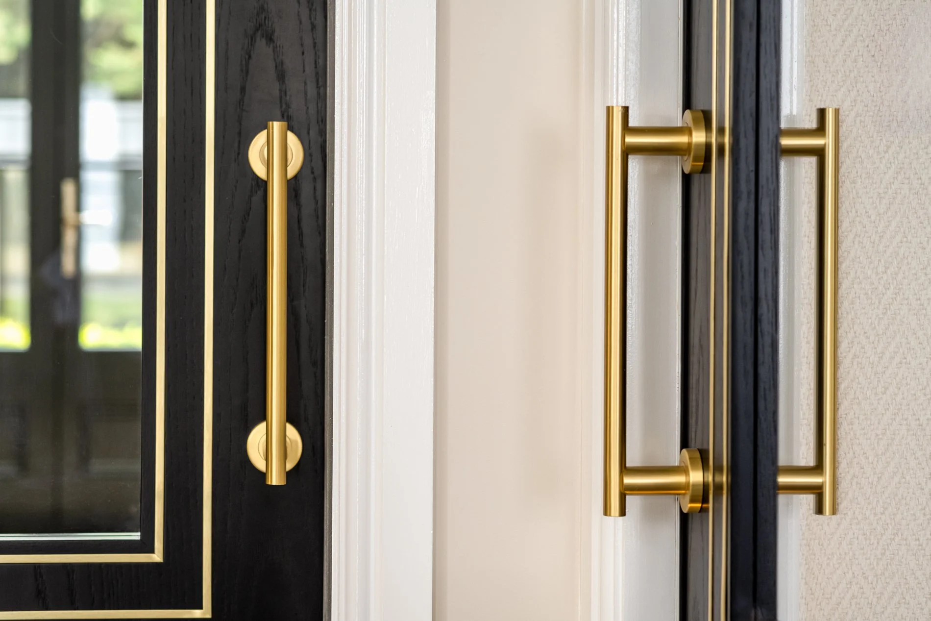A close-up detail of black interior doors with brass handles and glass panel detailing. The image highlights the contrast between dark timber, warm metal finishes and surrounding light wall finishes, showing the quality of the door hardware and mater