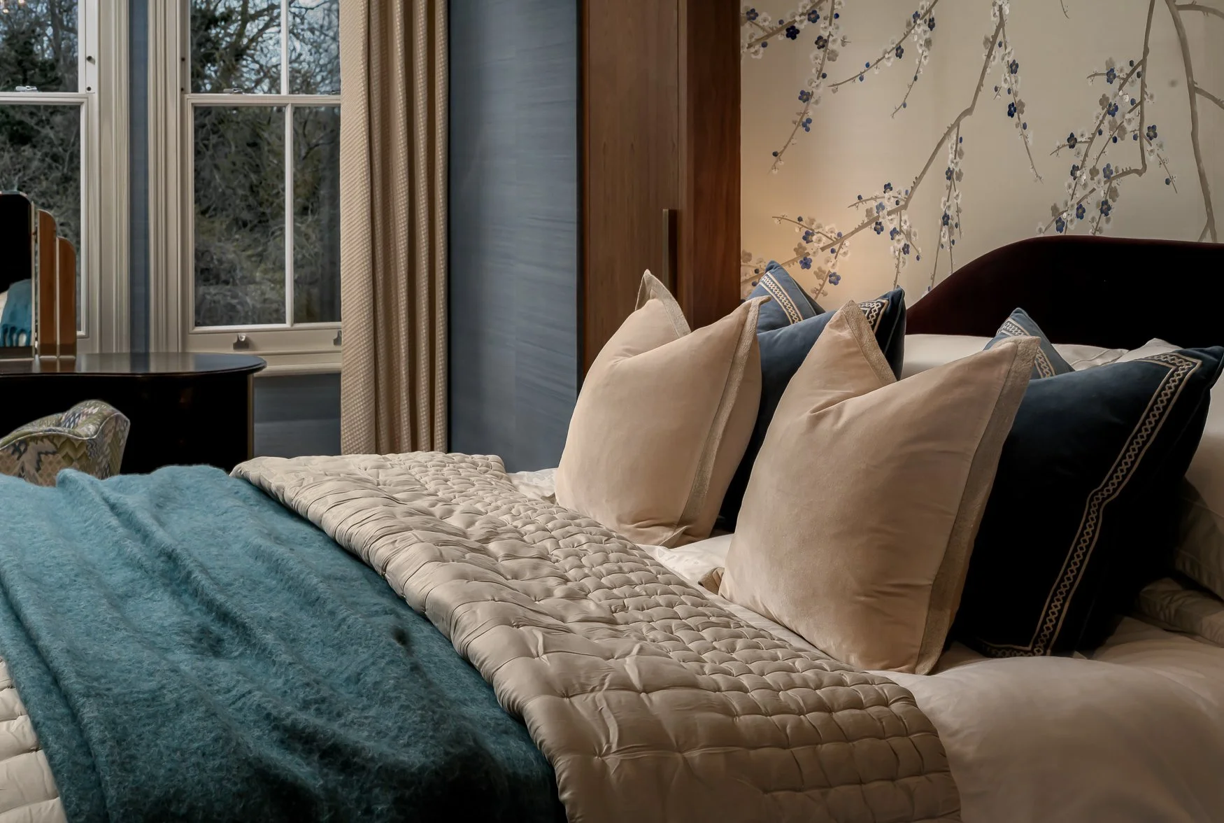 Layered bedroom interior with soft bedding, blue throw and custom wallcovering.