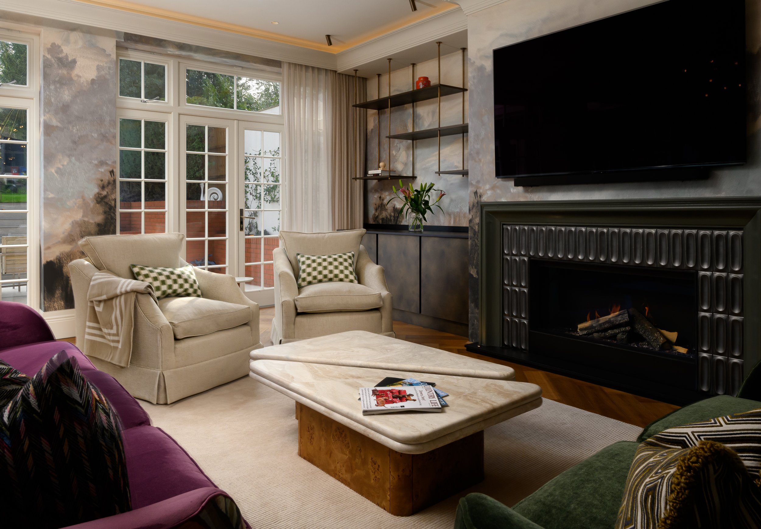 A luxury living room photographed in London, featuring a sculptural fireplace, layered seating, bespoke joinery, textured wall finishes, marble coffee tables and carefully styled details. The image captures the atmosphere, material choices and design