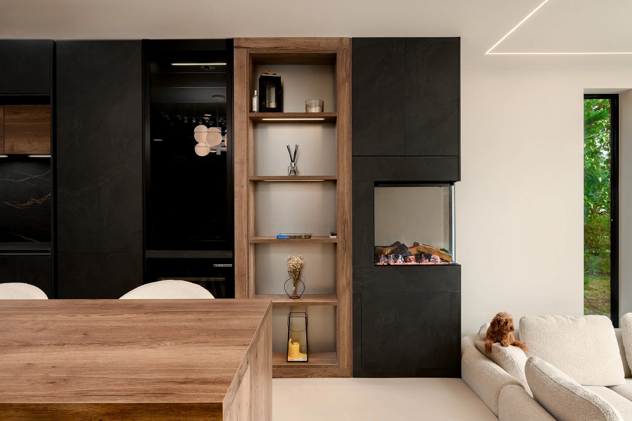 Modern open-plan living and kitchen interior with black cabinetry, timber shelving, integrated fireplace and white boucle sofa. Chelsea, London. KItchen by Kutchenhouse