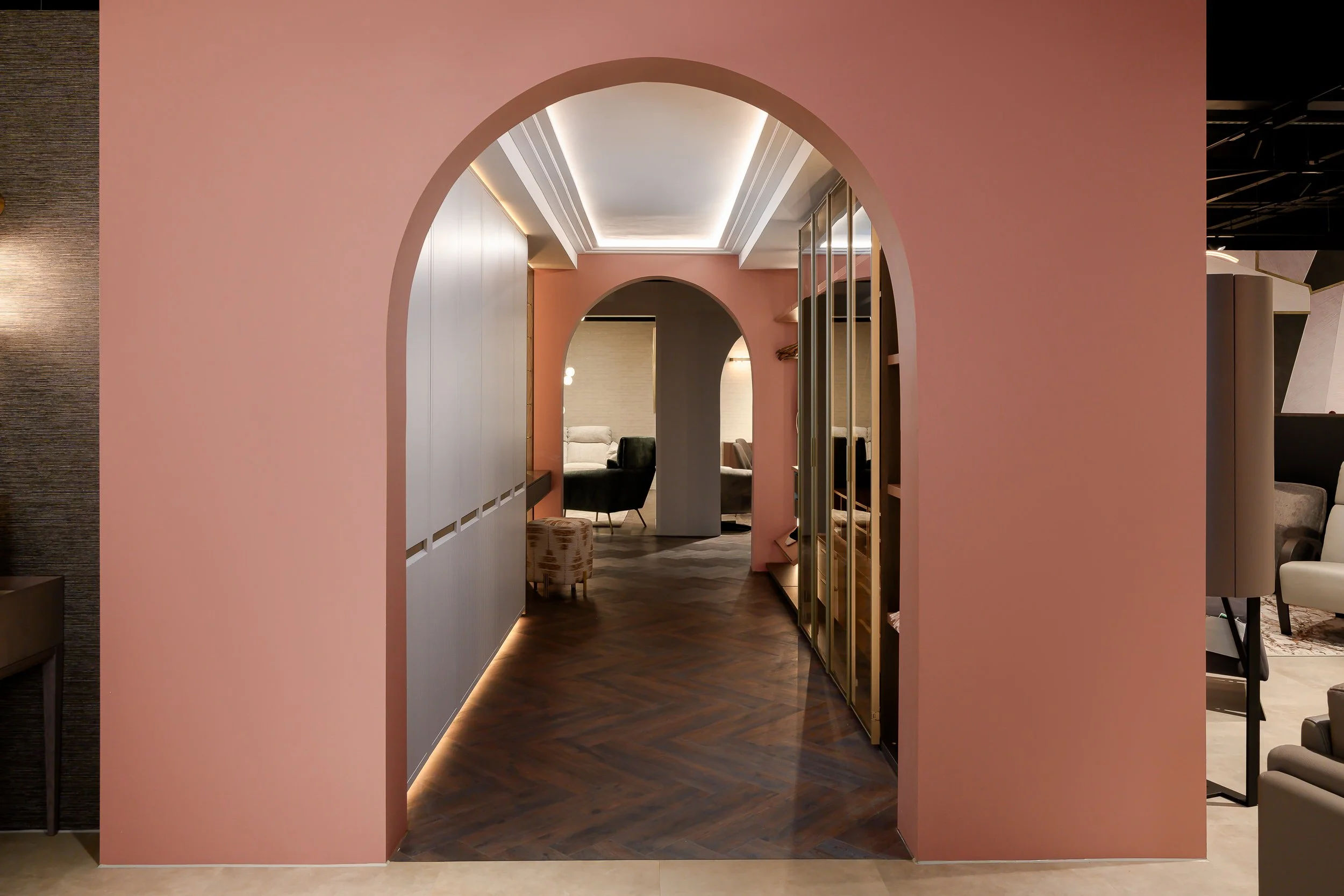 Interior view through pink archway leading into a lounge area with chairs and a table, warm lighting, and dark wood flooring.