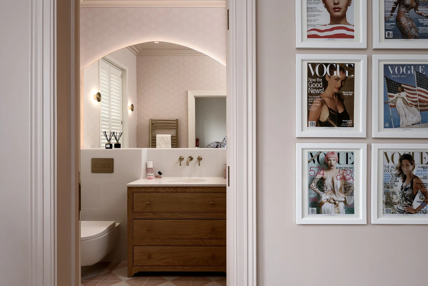View through doorway into pink ensuite bathroom with Vogue wall art and soft lighting.