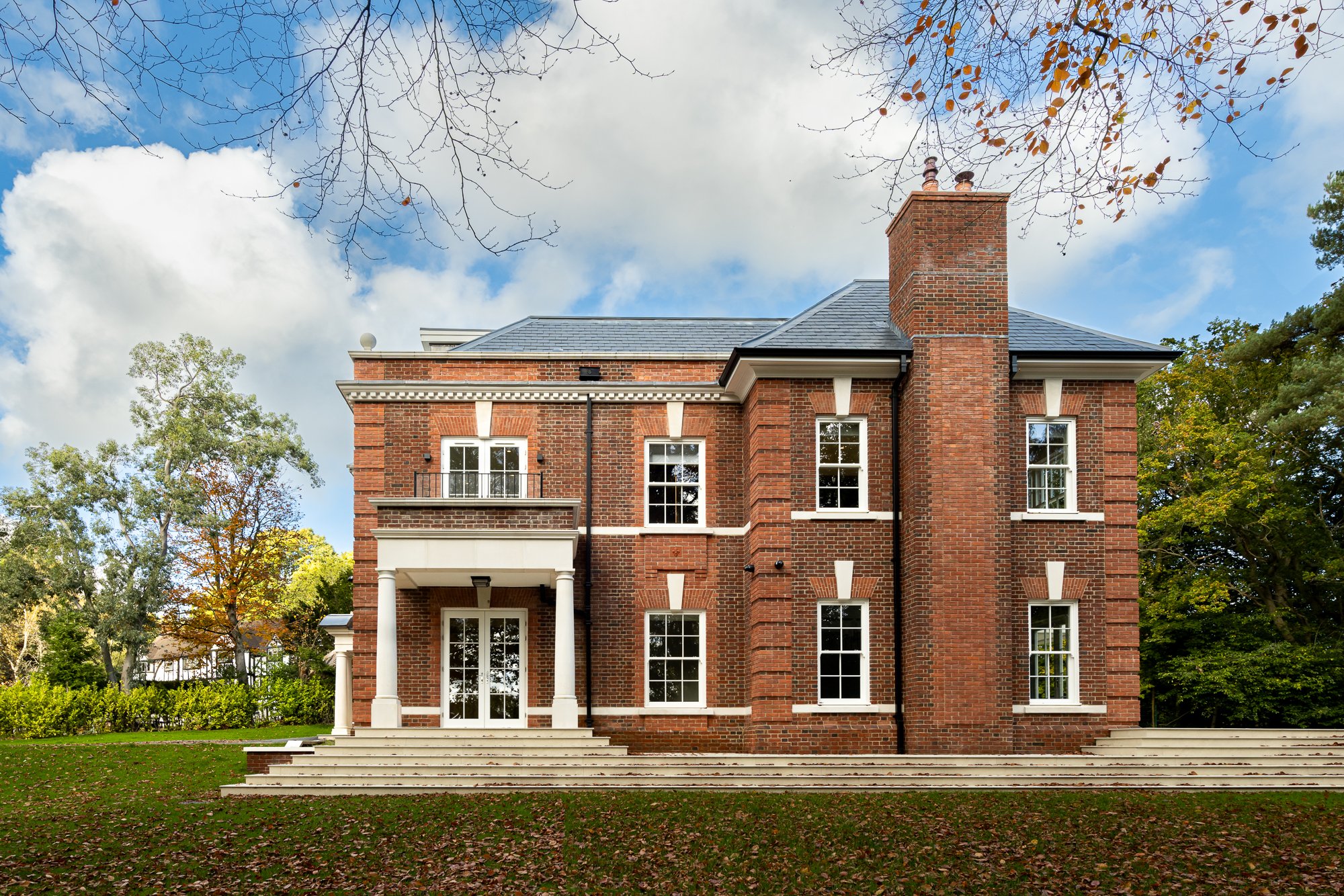 Side elevation architectural photograph of a large-scale premium residential development, showcasing external brickwork and structural masonry. The build features a prominent towering brick chimney stack, pre-cast stone window surrounds with sliding 