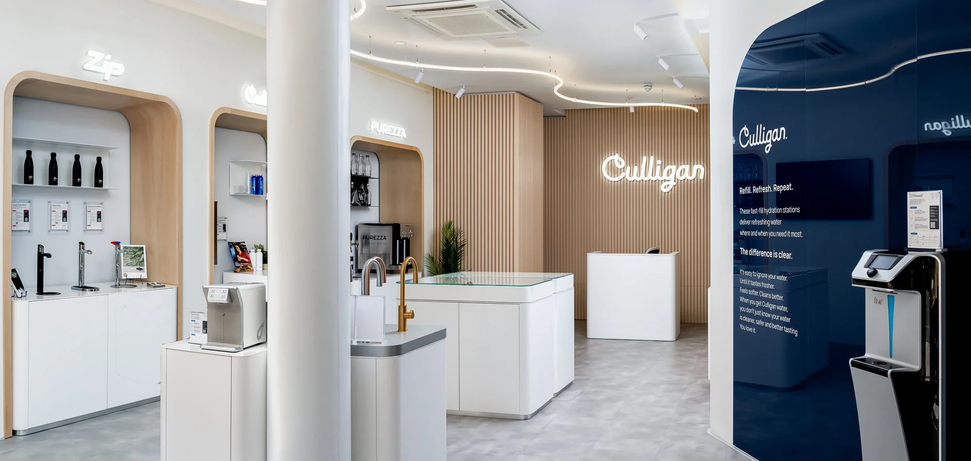 Interior of a Culligan water store featuring water refill stations, a sign with instructions, and sample bottles, with a modern and clean design.