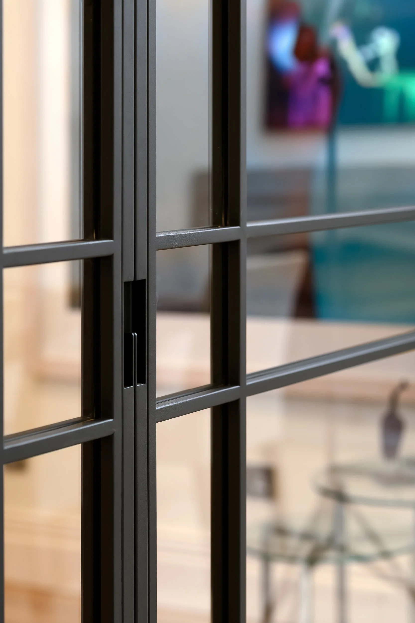 A close-up detail of a black framed glass door, showing the slim metal frame, glazing bars and handle recess. The shallow focus keeps attention on the door construction while softly showing the interior beyond.
