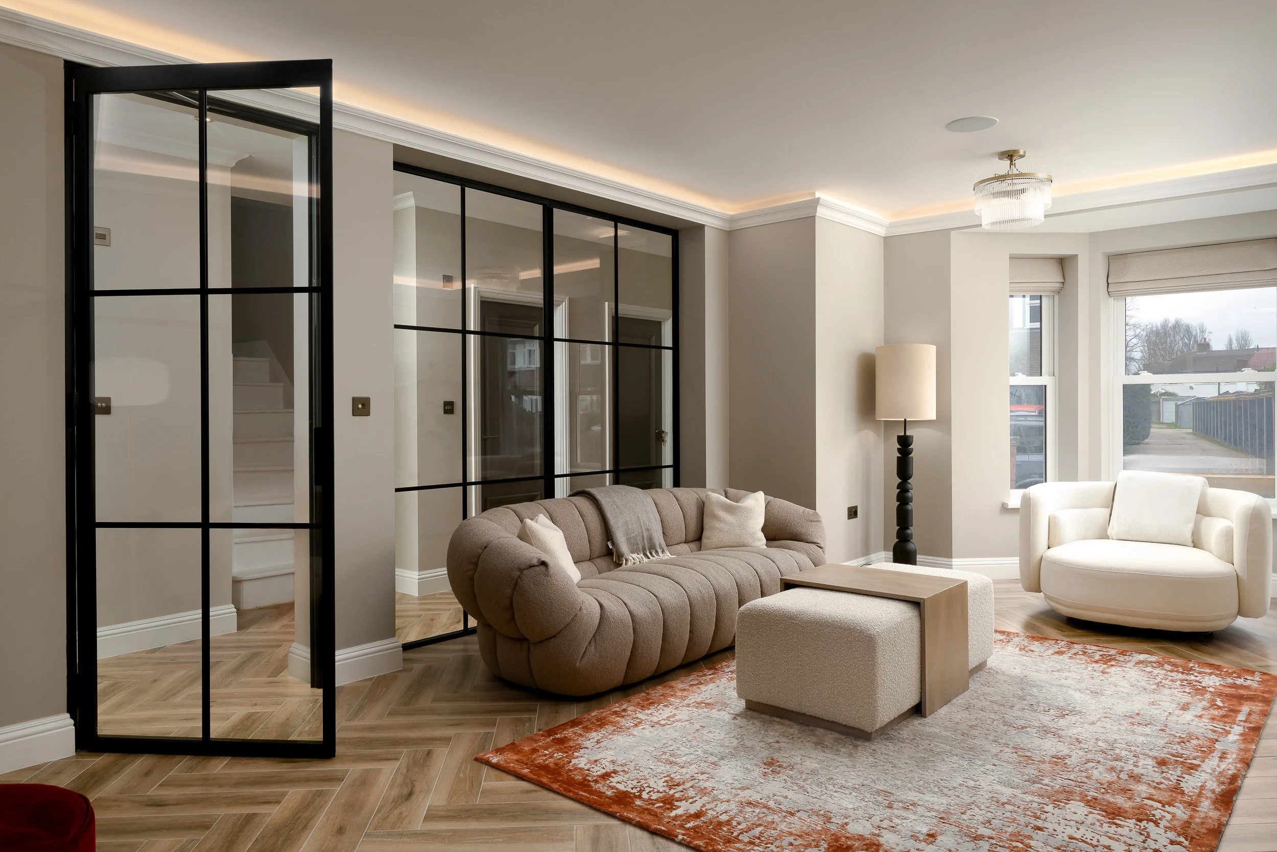 A modern London living room photographed with black framed glass partition doors behind the seating area. The image shows how internal glazing can divide spaces while keeping light, flow and visual connection between rooms.
