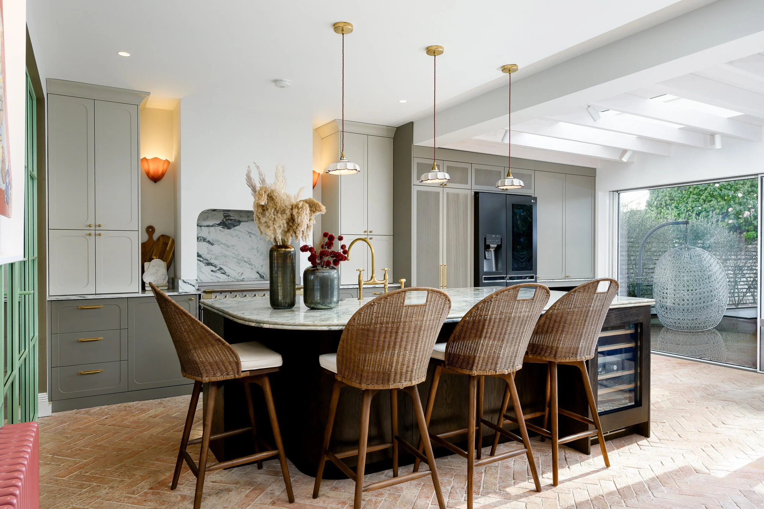 Wider view of the kitchen with bar chairs, integrated wine fridge and rounded island