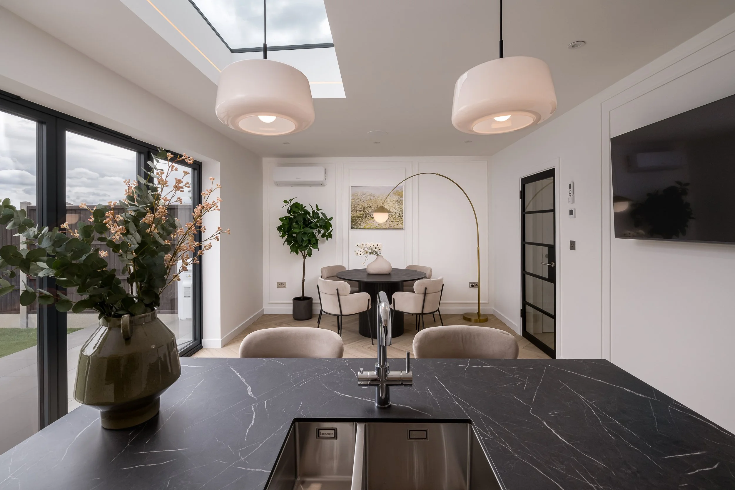 Reverse-angle architectural photograph capturing an open-plan structural kitchen and dining extension. Shot for main contractors and architectural firms to demonstrate spatial layout optimization, featuring an overhead structural skylight installatio
