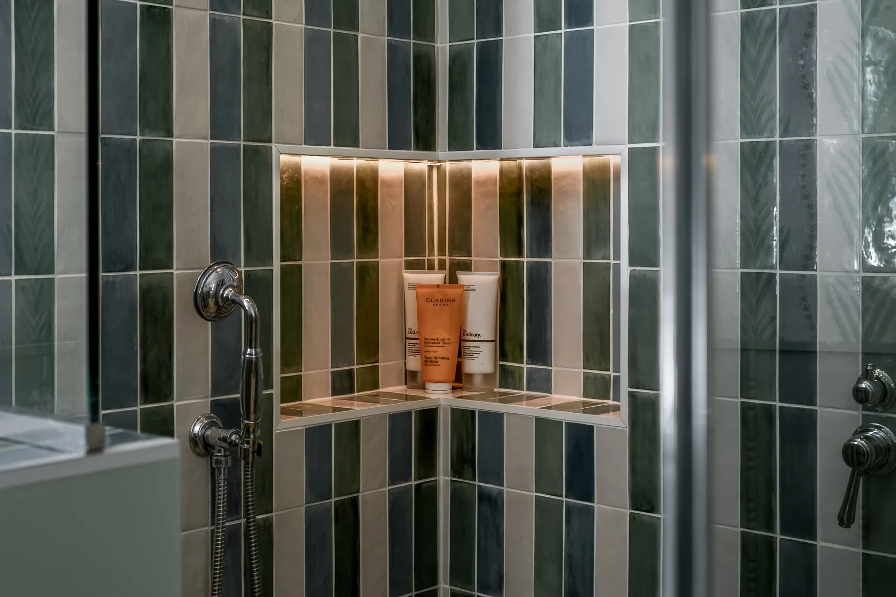 Green tiled shower with brass fittings, glass screen and integrated shelf lighting.