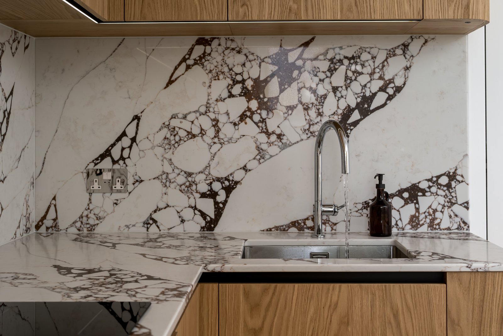 Close interior photograph of timber cabinetry, sink and dramatic veined stone splashback in a bespoke kitchen.