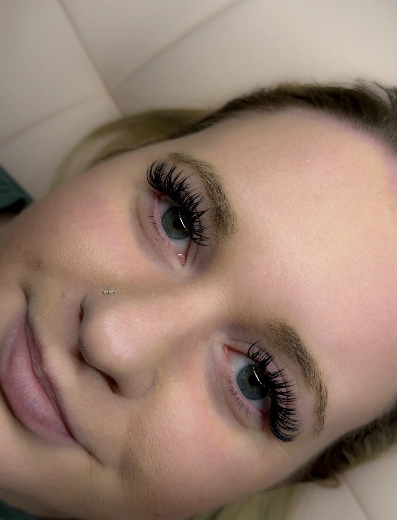Close-up of a woman lying down with striking blue eyes and long, black eyelashes.