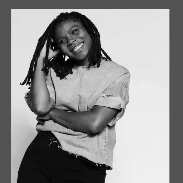 Smiling Black woman with locs posing in a casual T-shirt and pants, black-and-white portrait