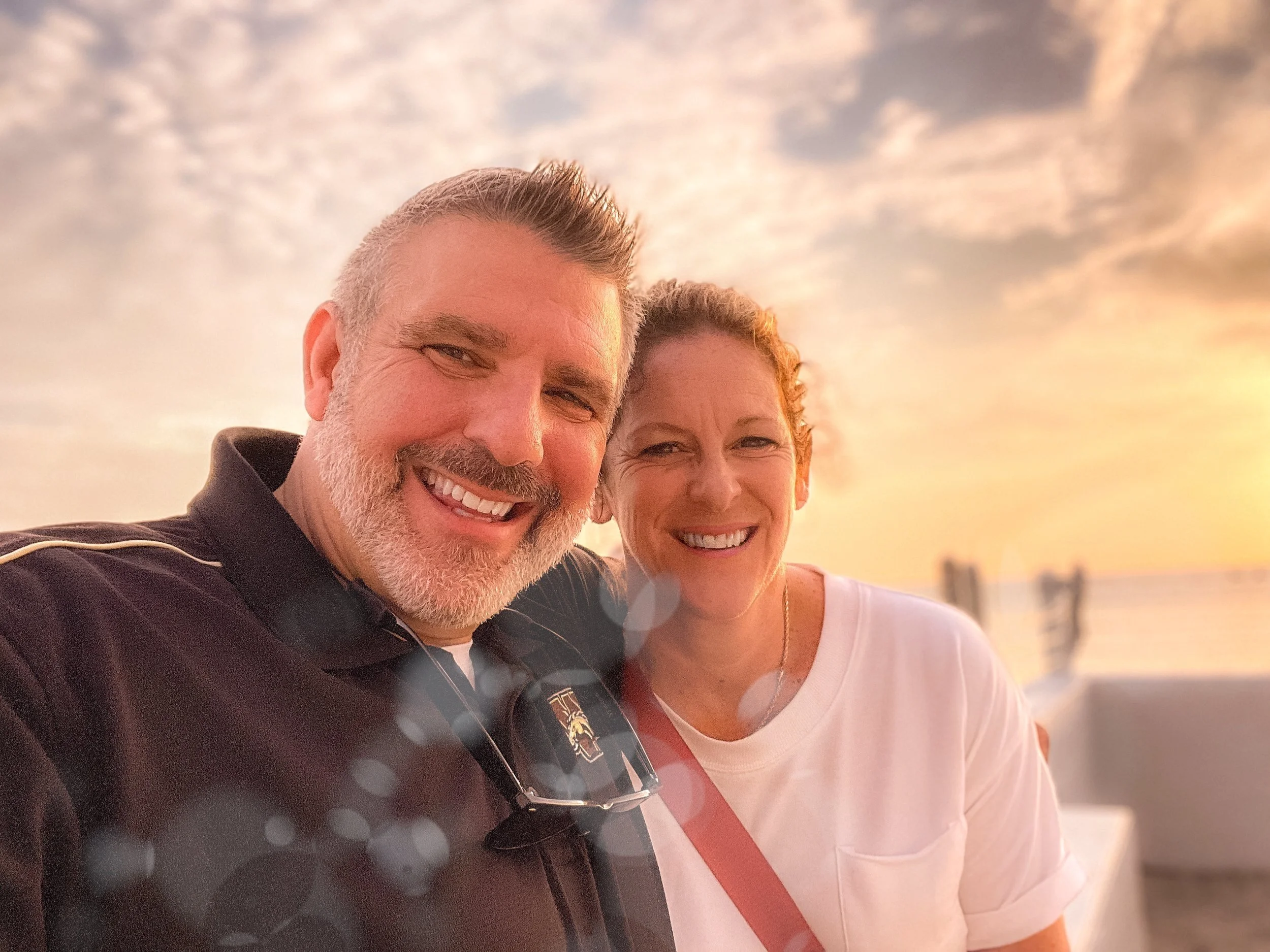 Smiling couple taking a selfie against a sunset background.