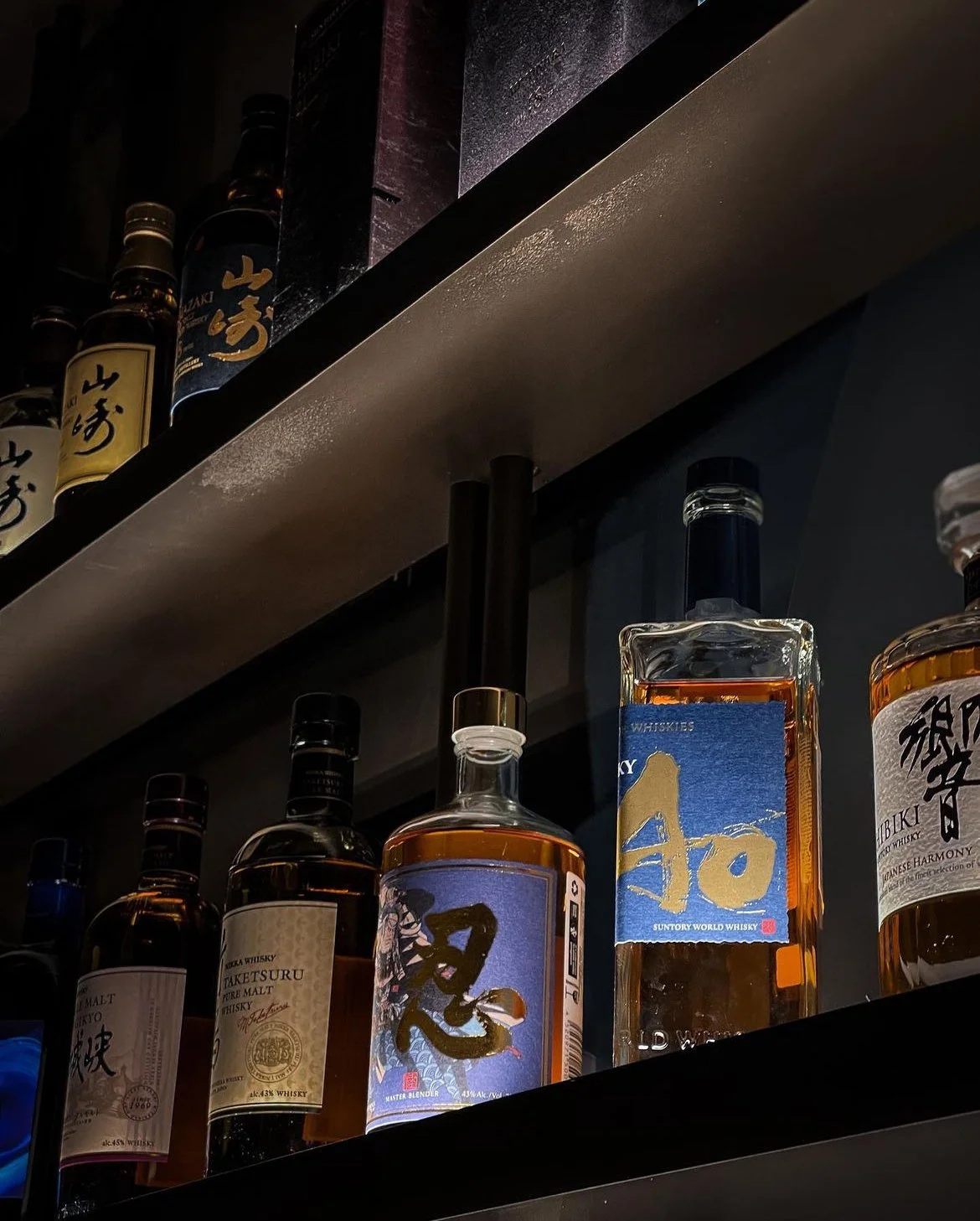 Various bottles of whiskey on shelves, including brands with Japanese labels and artwork.