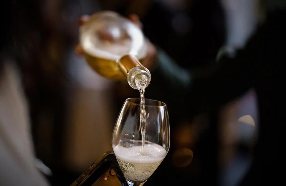 A person pouring sparkling wine or champagne into a wine glass in a dimly lit setting.