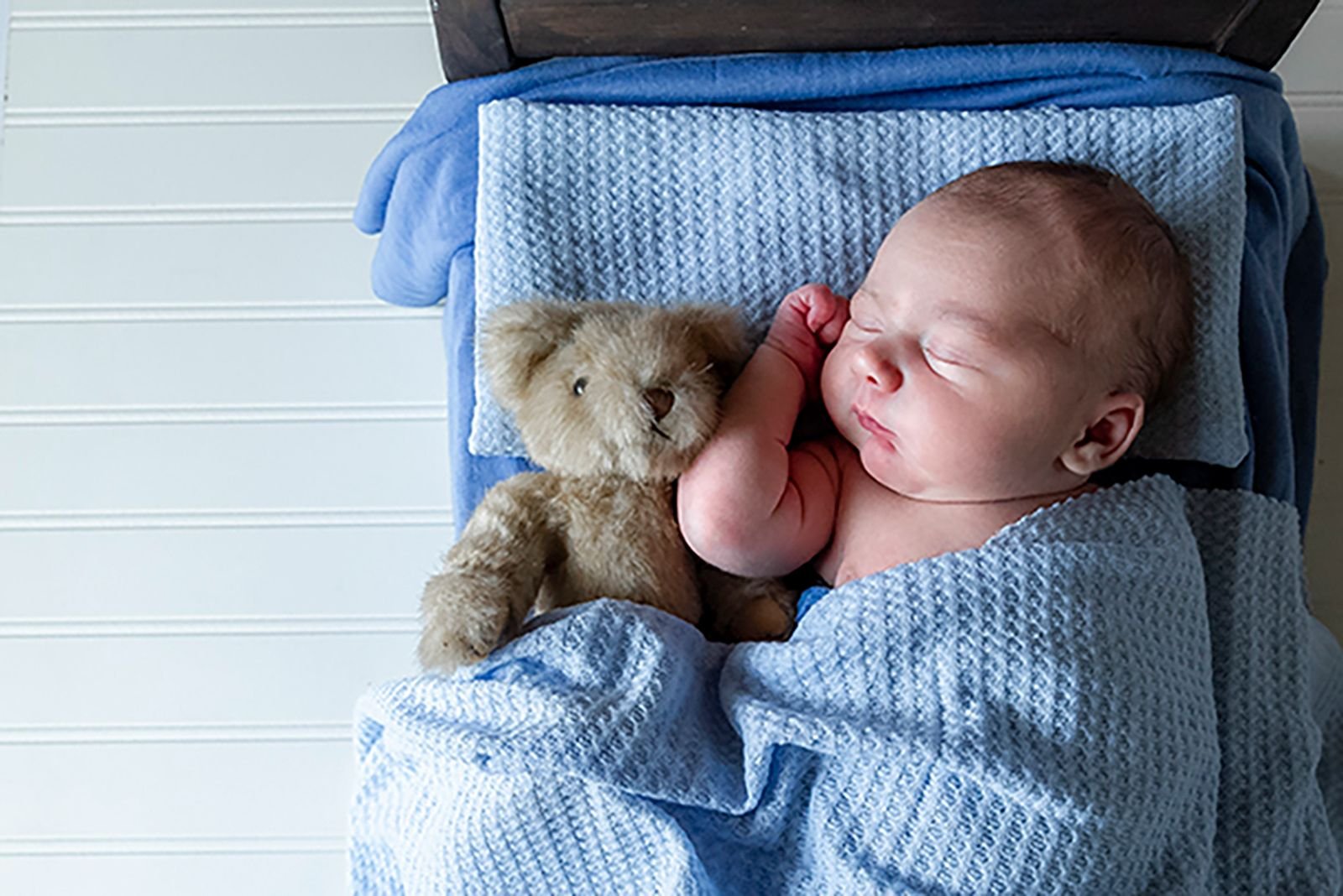newborn laying on a newborn bed with his teddy bear