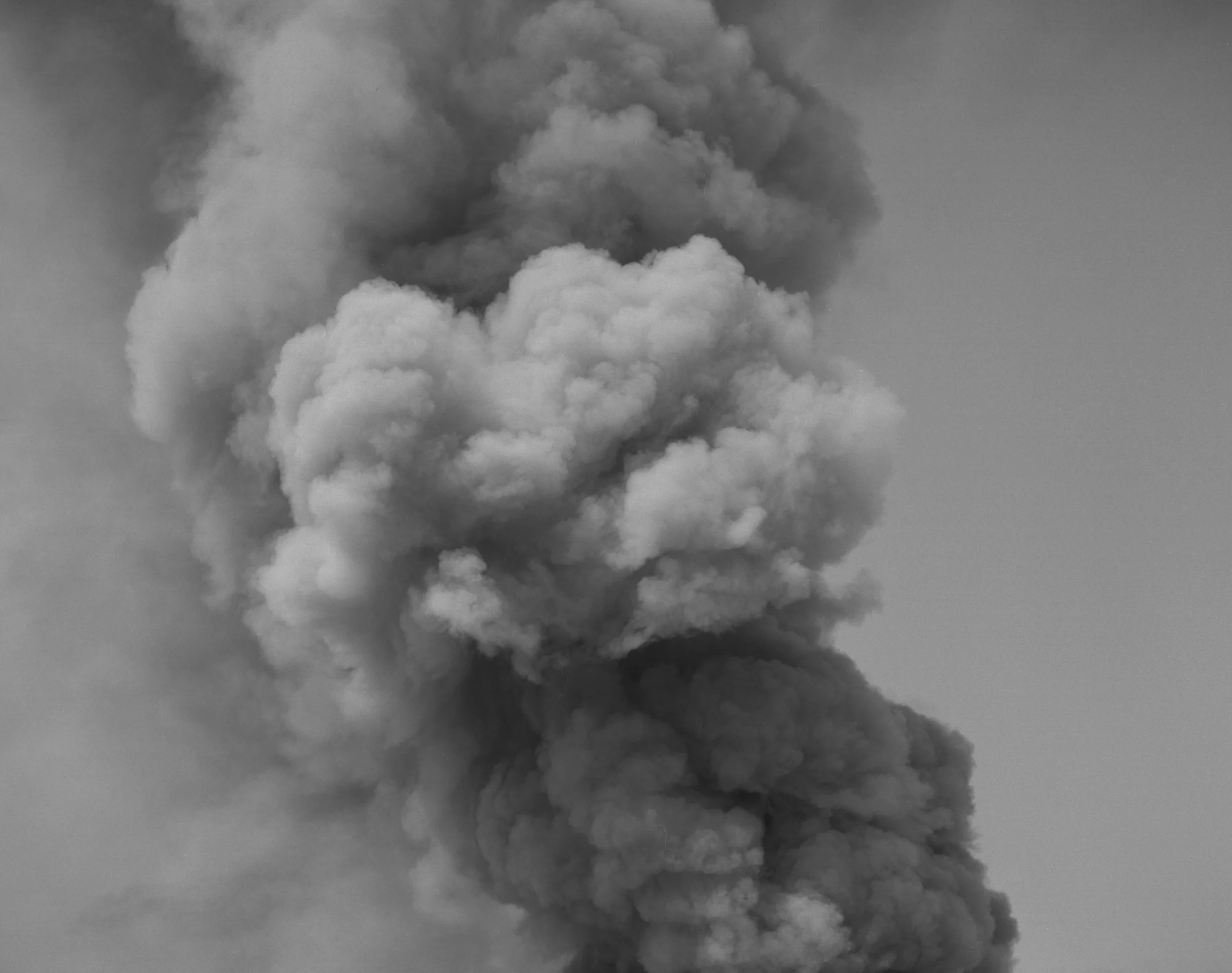 A black and white photograph of large, billowing clouds in the sky, with a mixture of light and dark shades.