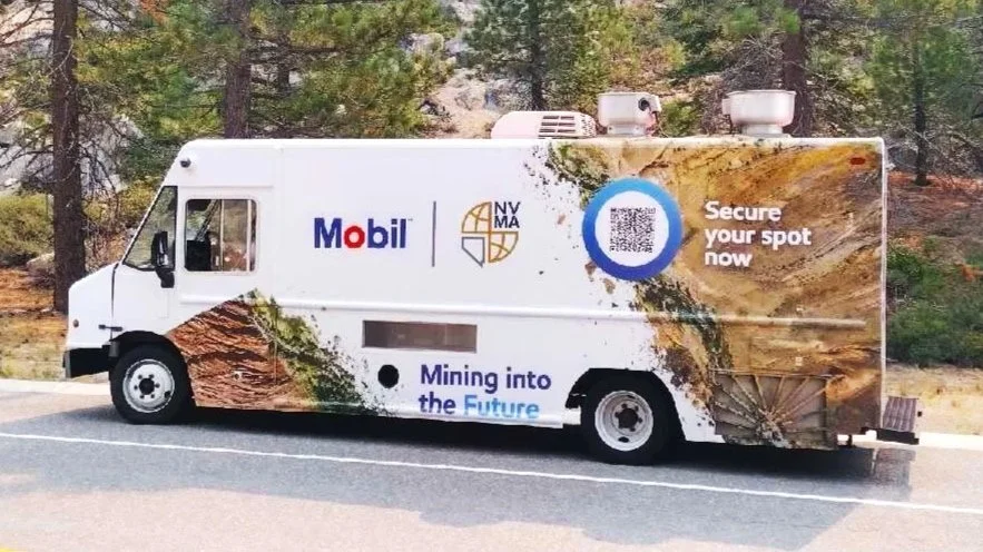 A mobile billboard truck parked on the side of a road, featuring an advertisement for mining and the phrase 'Mining into the Future.'