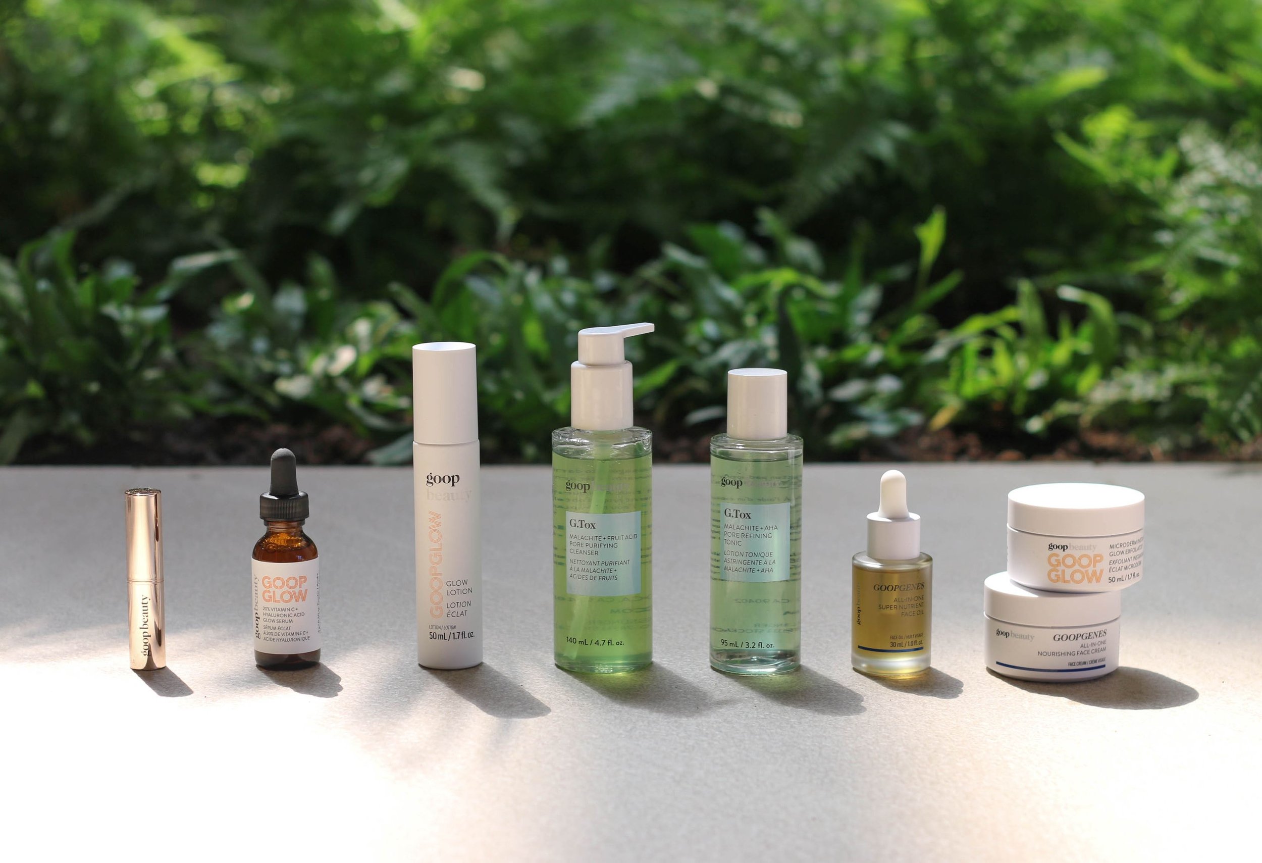 8 beauty products lined up in a row with green foliage backdrop