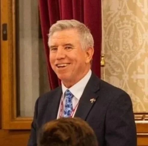 A smiling man wearing a white dress shirt against a plain white background.
