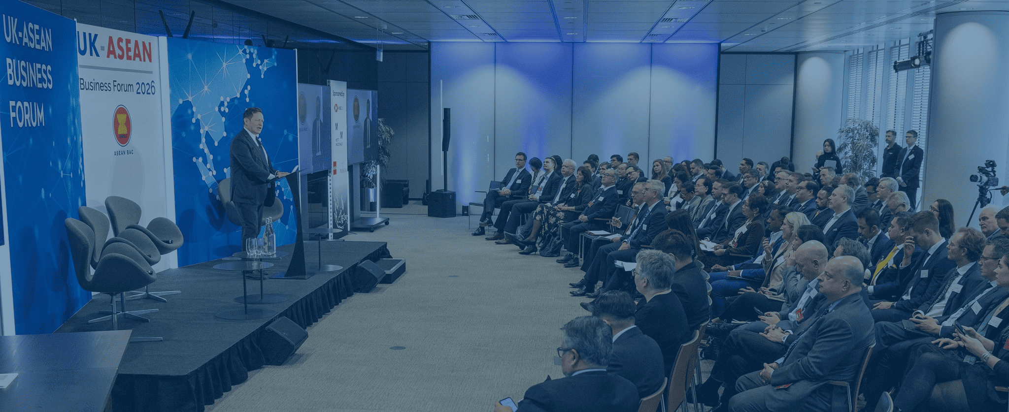 Group of eight professionals standing in front of banners that read "UK-ASEAN BUSINESS COUNCIL". The background features a colorful artwork and text about the arts.