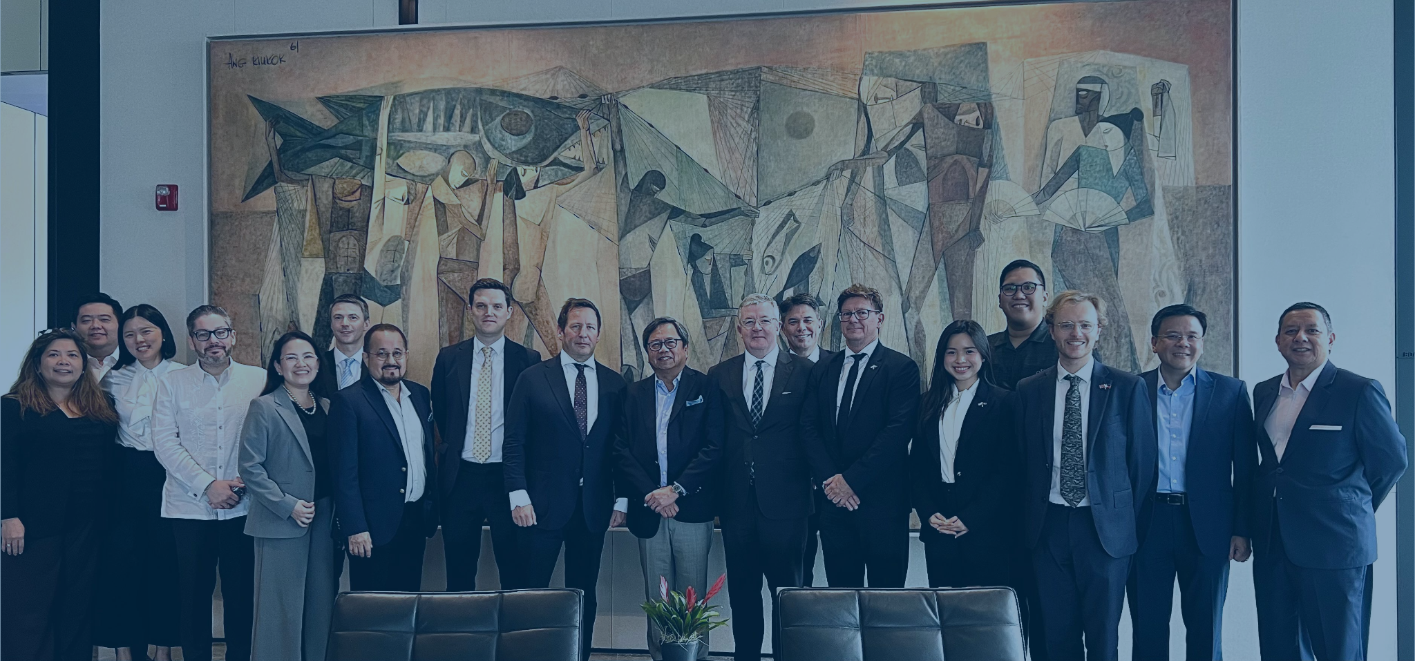 Group of diverse professionals in business attire standing in front of a large abstract mural in a conference room.