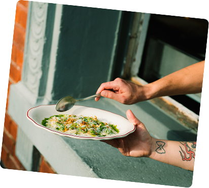 A person holding a plate of food with a spoon, standing near a window in a kitchen.