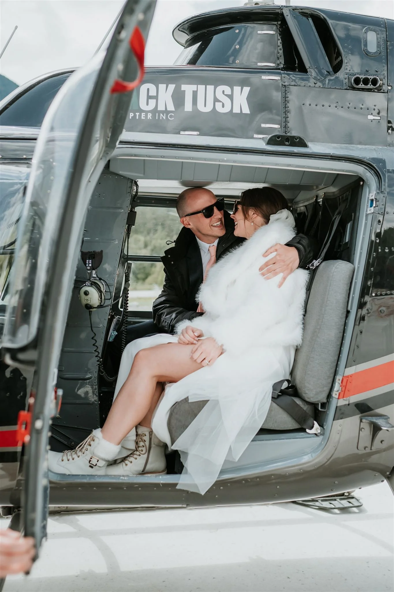 a couple in the back seat of a helicopter wearing a suit and wedding gown