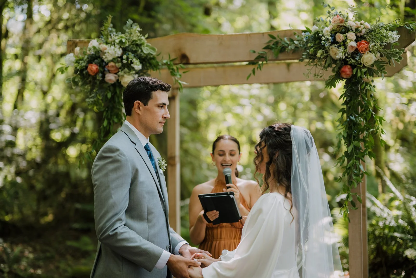 A bride and groom standing at the altar, during their wedding ceremony. In the forest.