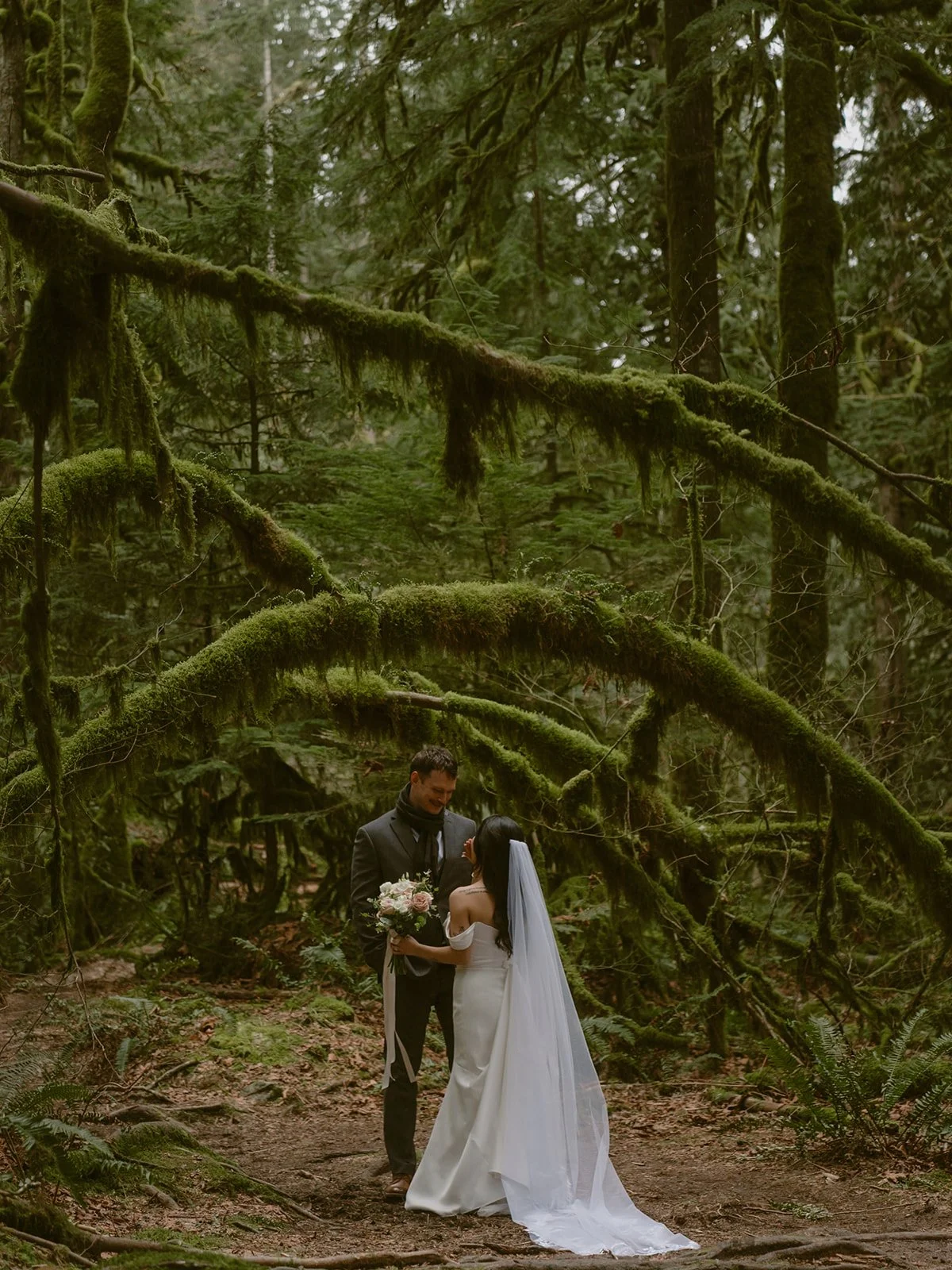 A bride and groom in the forest, under natural lichen-covered arches