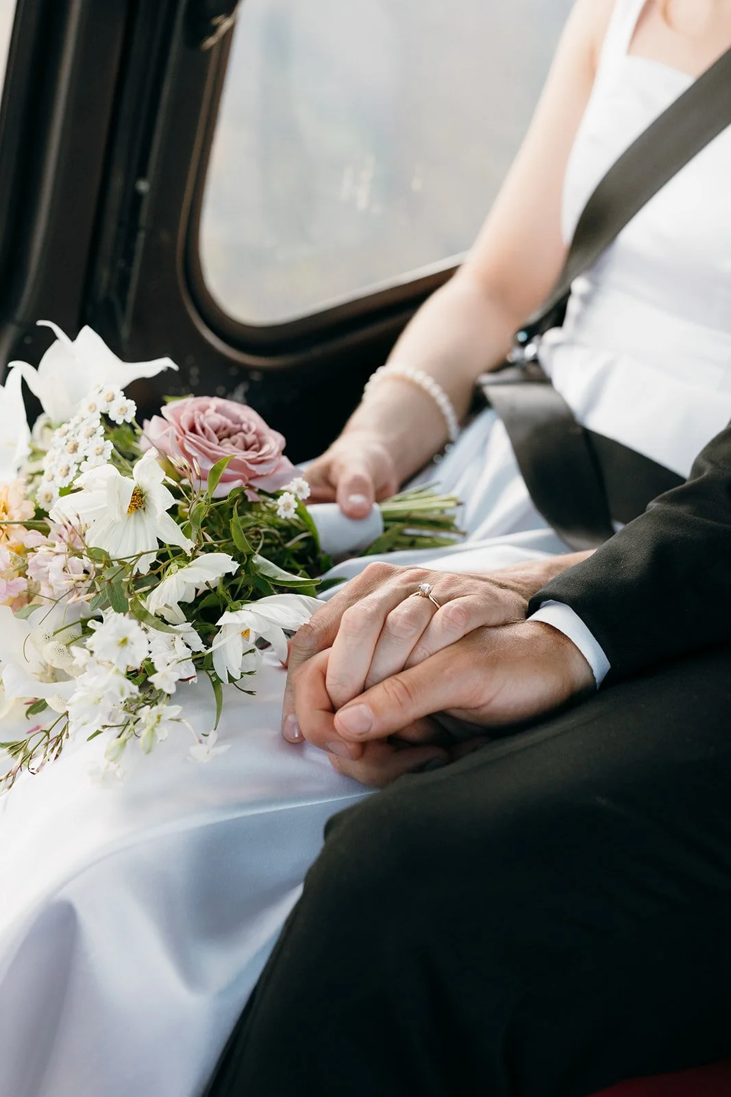 A couple holding hands in their bridal clothes, sitting in a helicopter