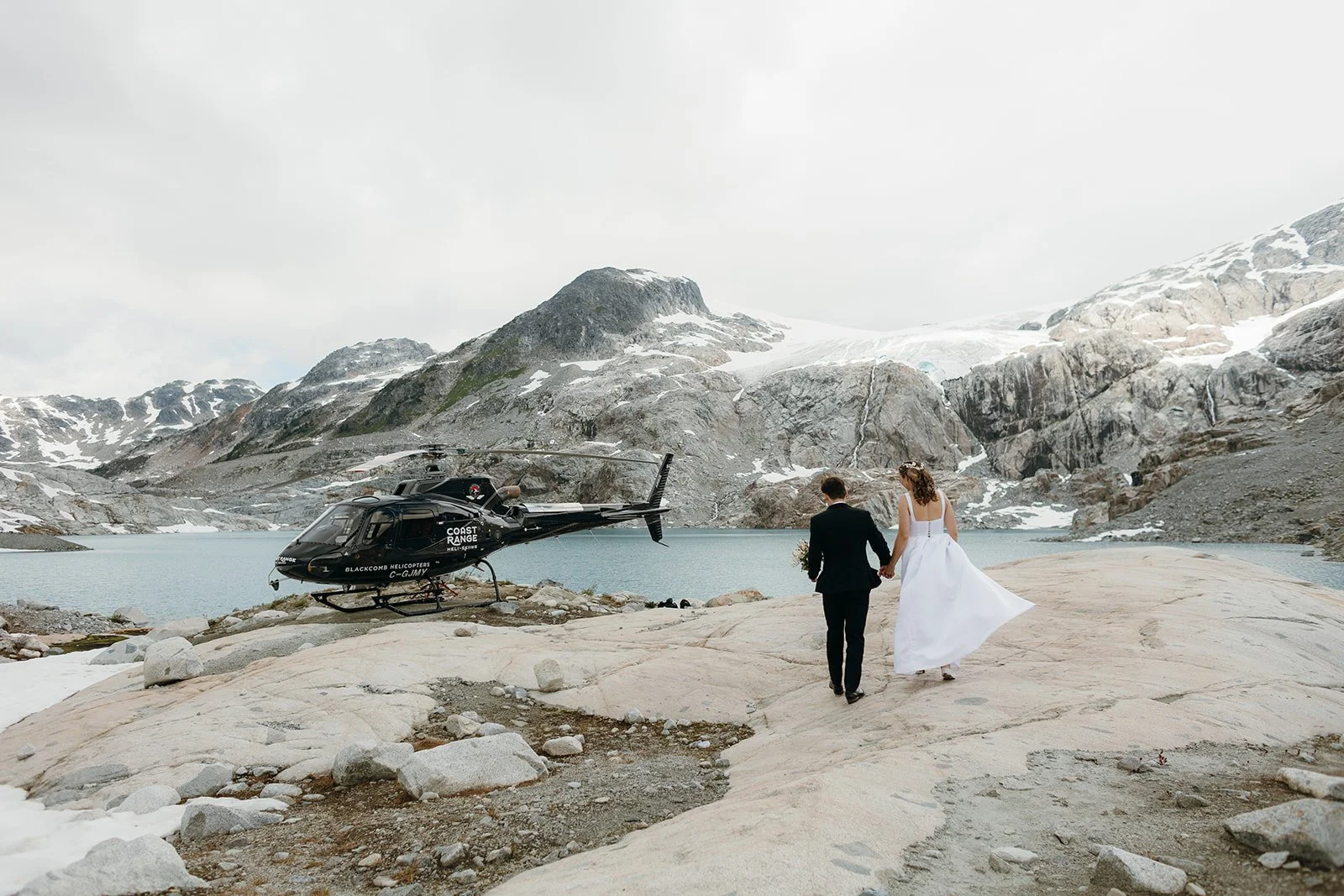 A bride and groom in the alpine, walking towards a helicopter