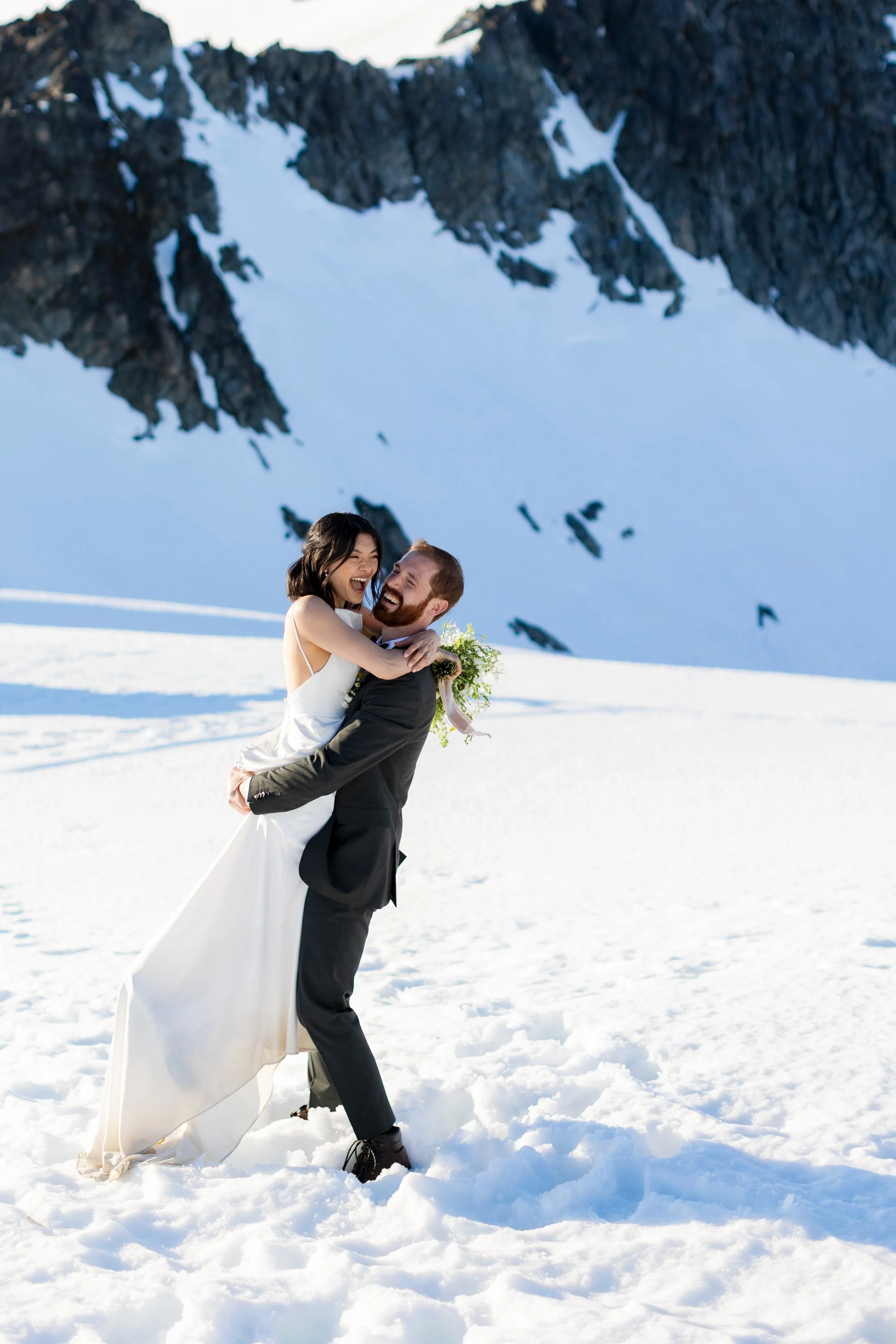 A couple in their wedding clothes hugging, with snow in the background
