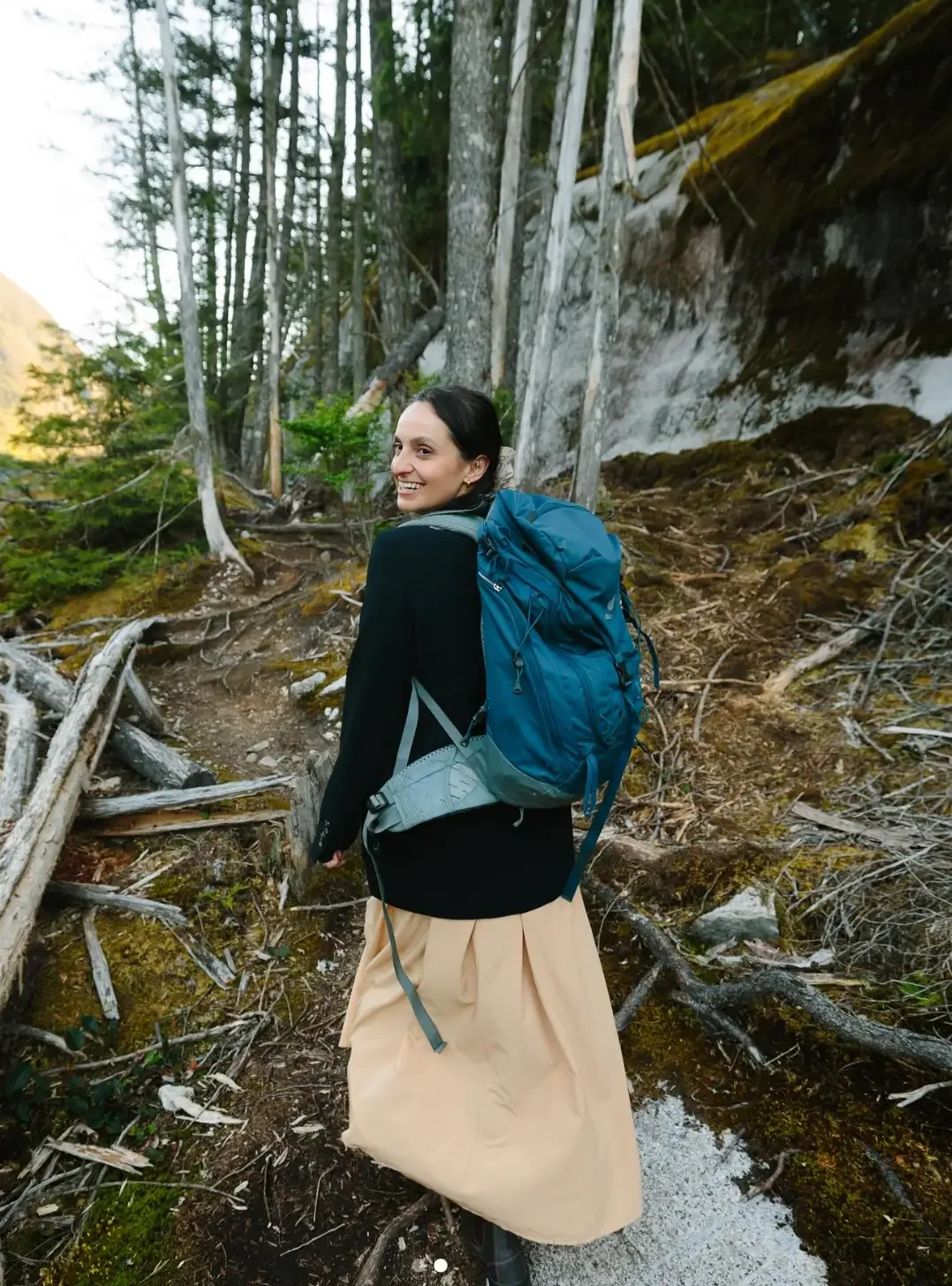 Jude hiking on a forest trail with a blue backpack, smiling and turning back.