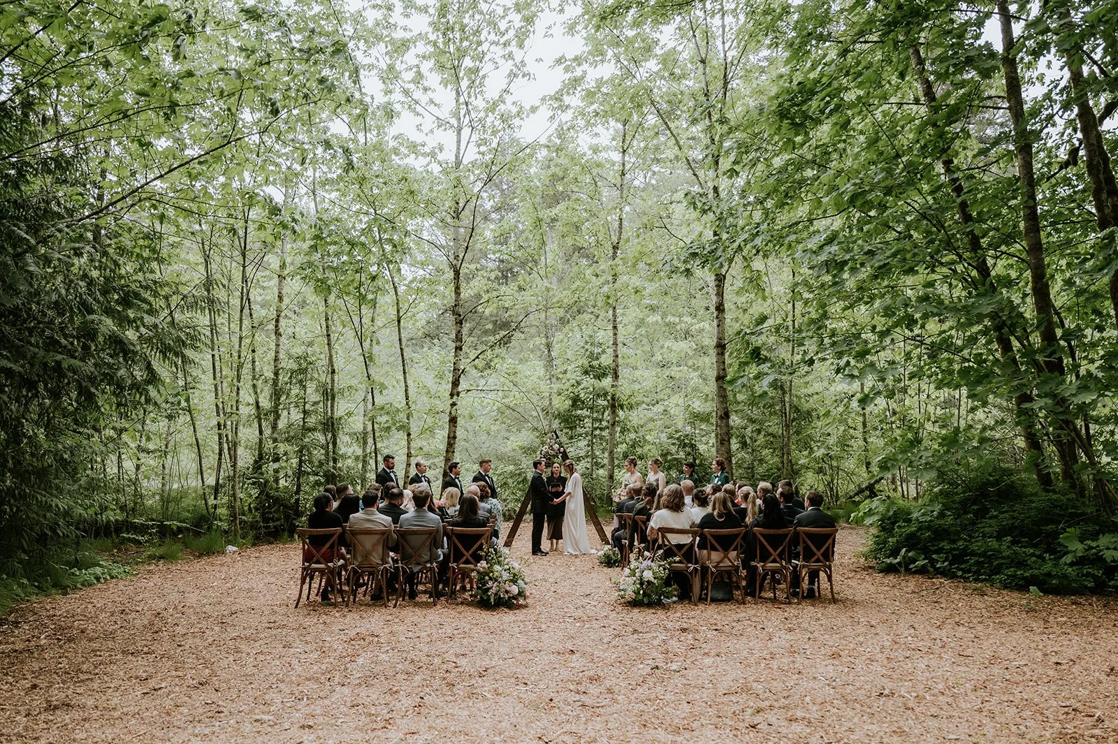 A wedding ceremony taking place in a clearing in the forest - with the bride and groom at the altar, and guests seated listening to the ceremony