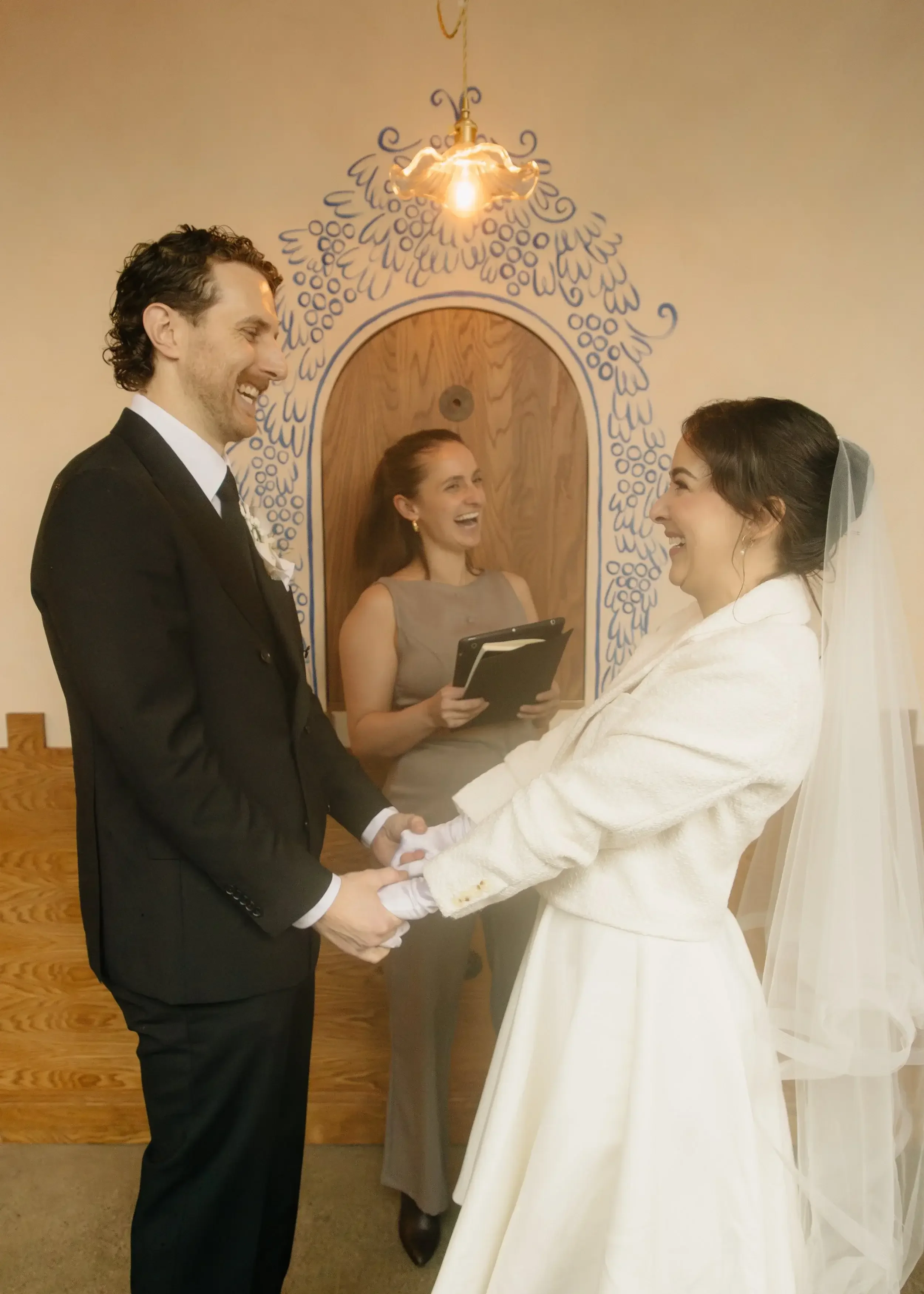 a couple laughs and holds hands as jude douglass their wedding ceremony officiant stands behind them