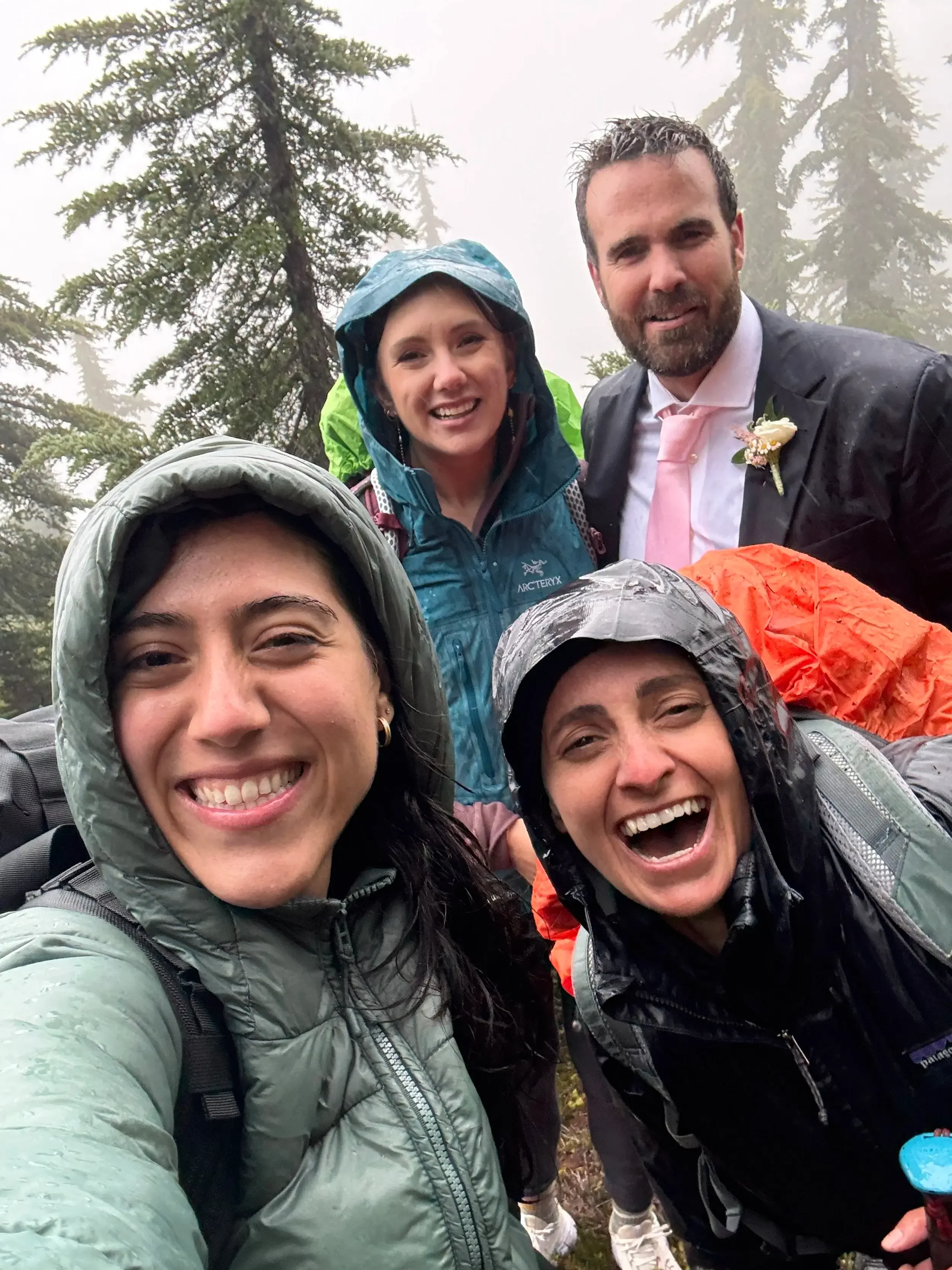 jude, the photographer, and bride and groom laugh together in the rain